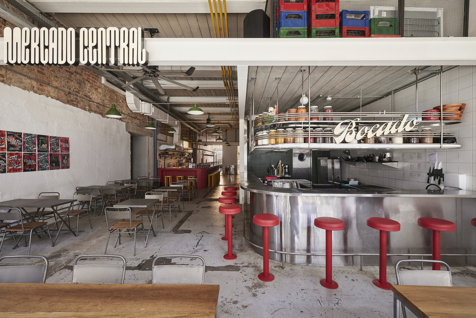 Curved stainless steel counter with red stools and a hanging jar shelf, beside a white-painted brick wall and metal tables