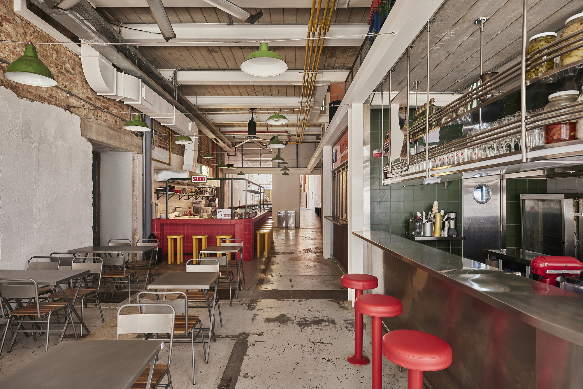 Long view down the dining room past red stools, green pendant lamps and a red tiled bar at the far end