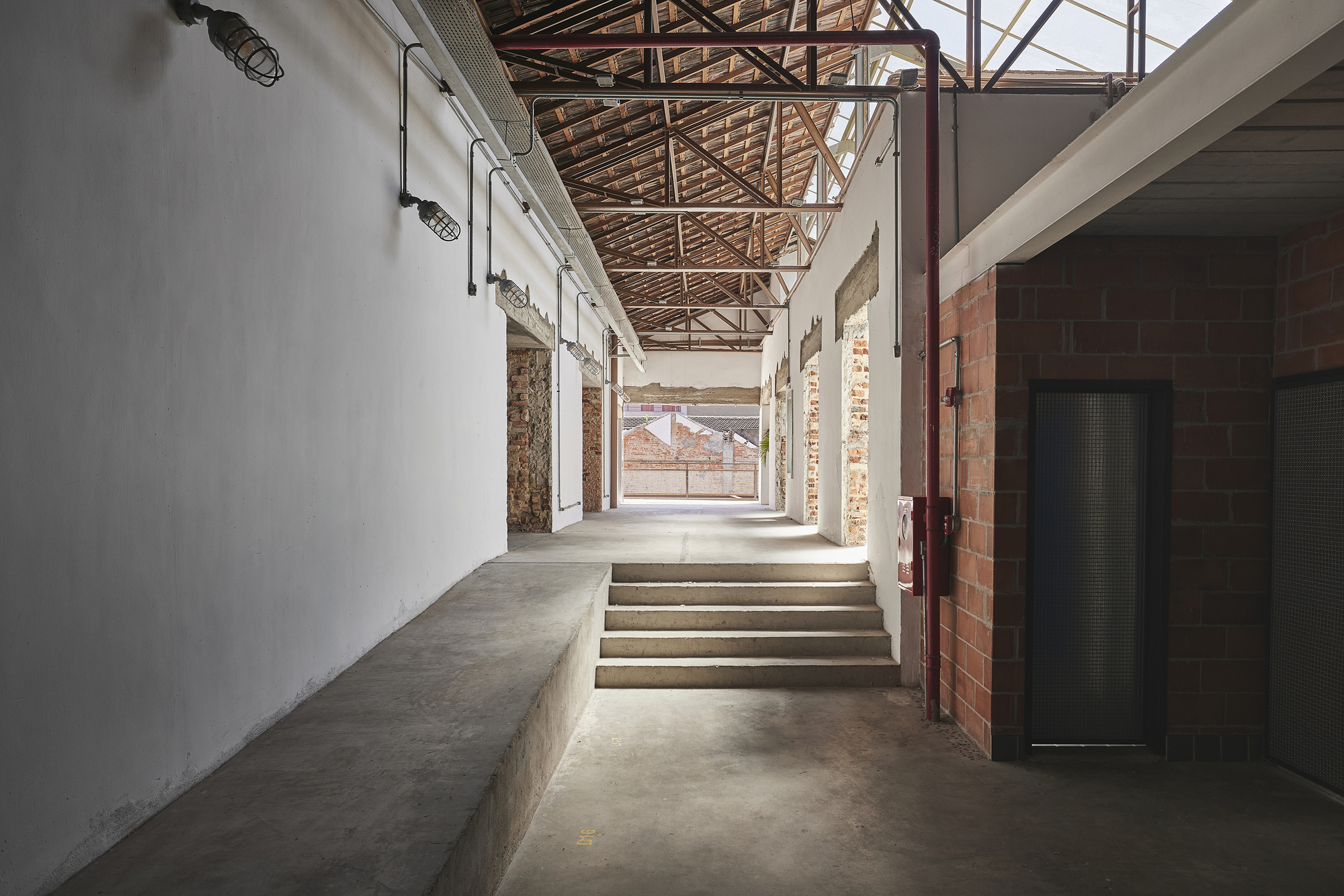 Concrete steps and a raised bench along a white wall, with red pipework and skylit timber trusses overhead