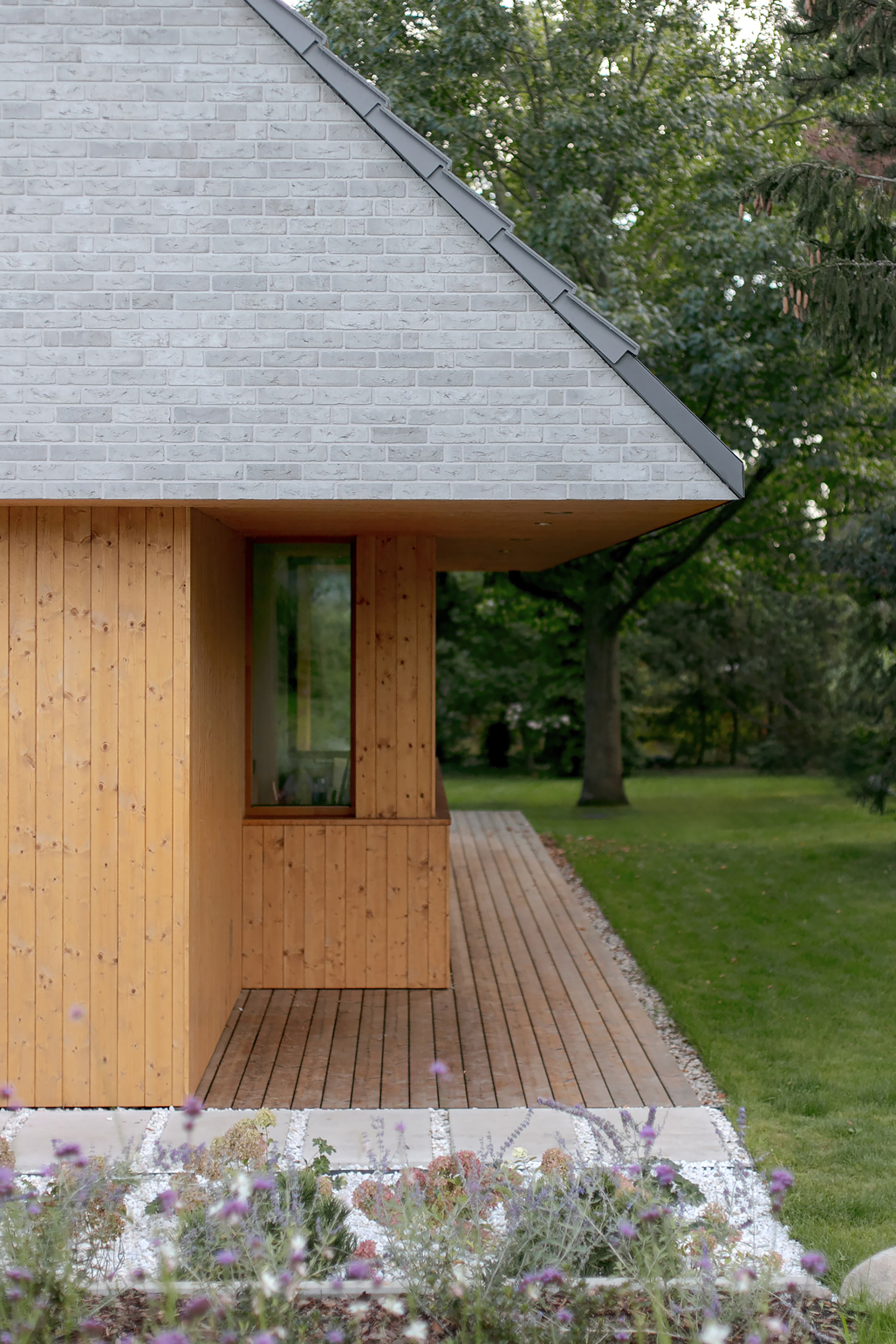 Side of the timber-clad volume with a deck running along it and lavender in the gravel bed in front