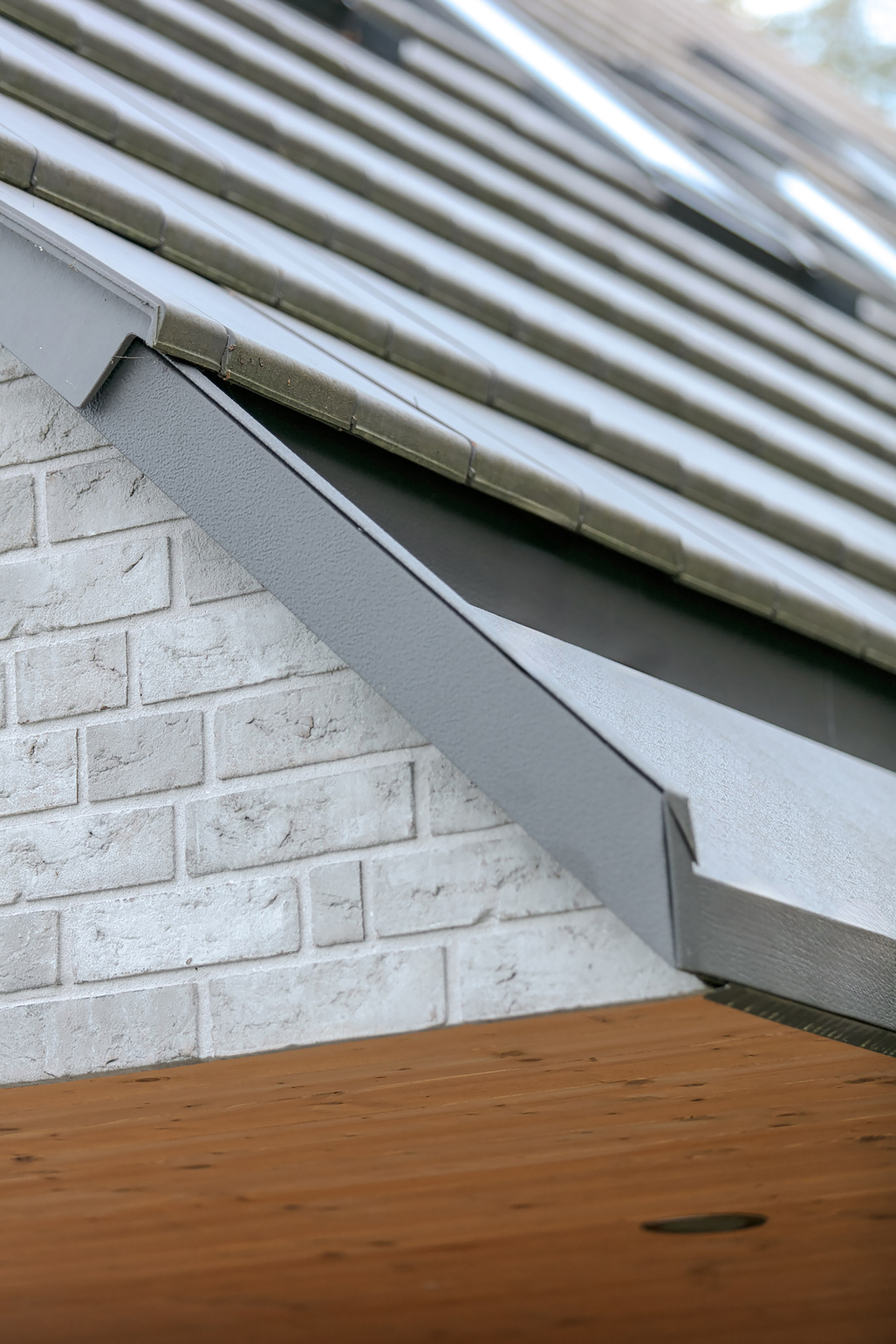 Close-up of the grey metal verge flashing where the tiled roof meets white-washed brick gable above a timber soffit