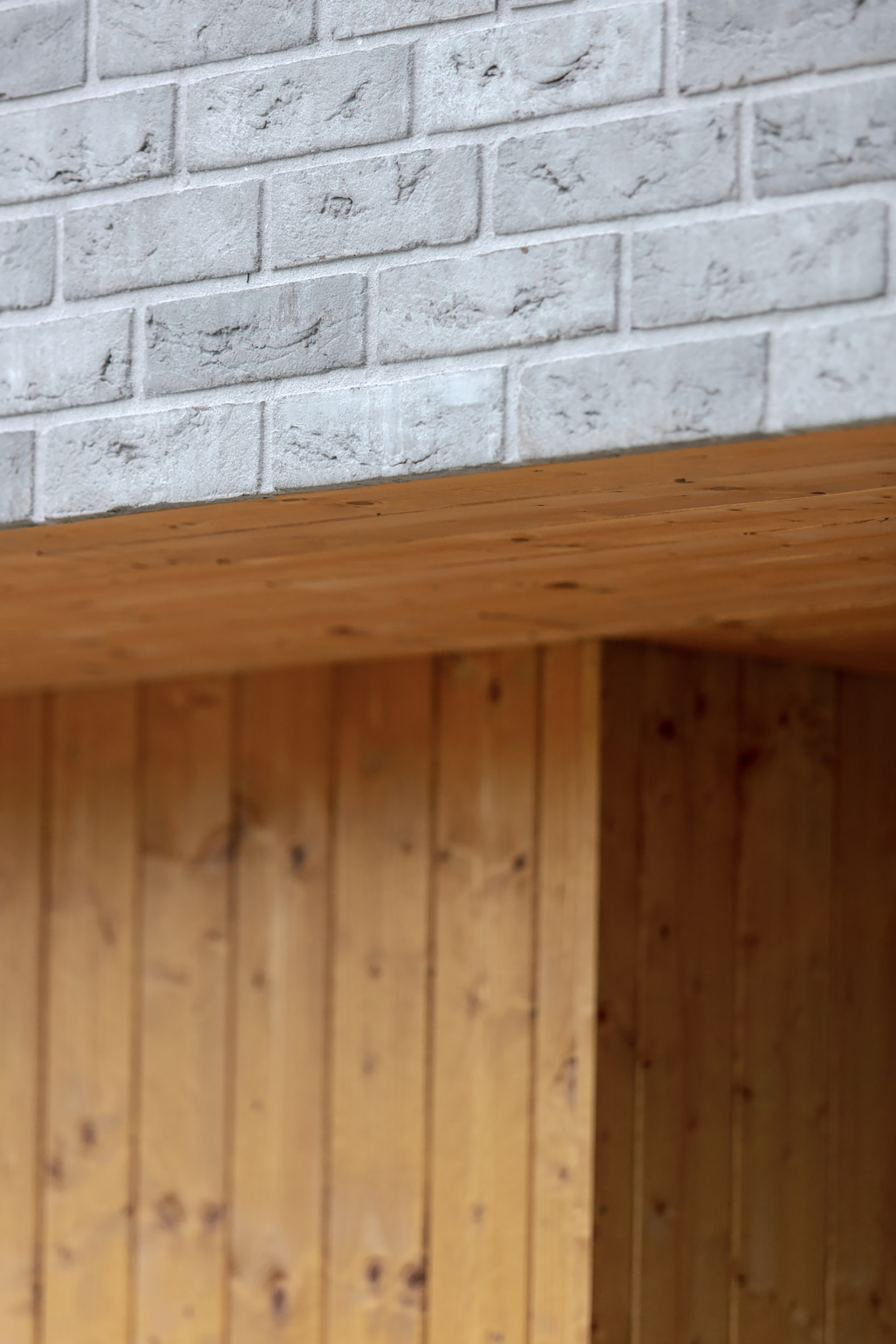Close-up of pale grey brick resting on a timber soffit above vertical pine cladding with visible knots