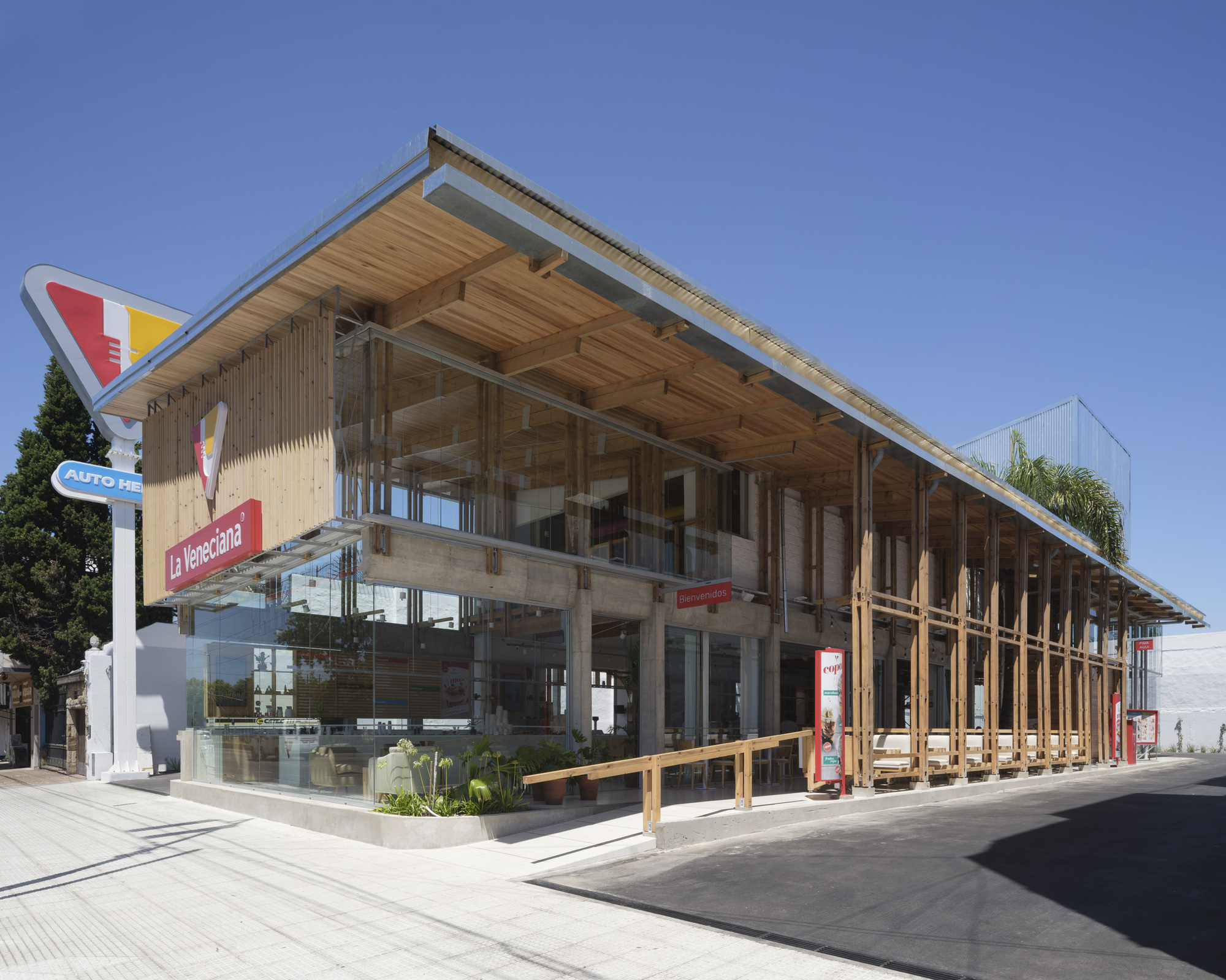 Corner view of the two-storey timber and glass shopfront with a sloping wood-lined roof, under a clear blue sky