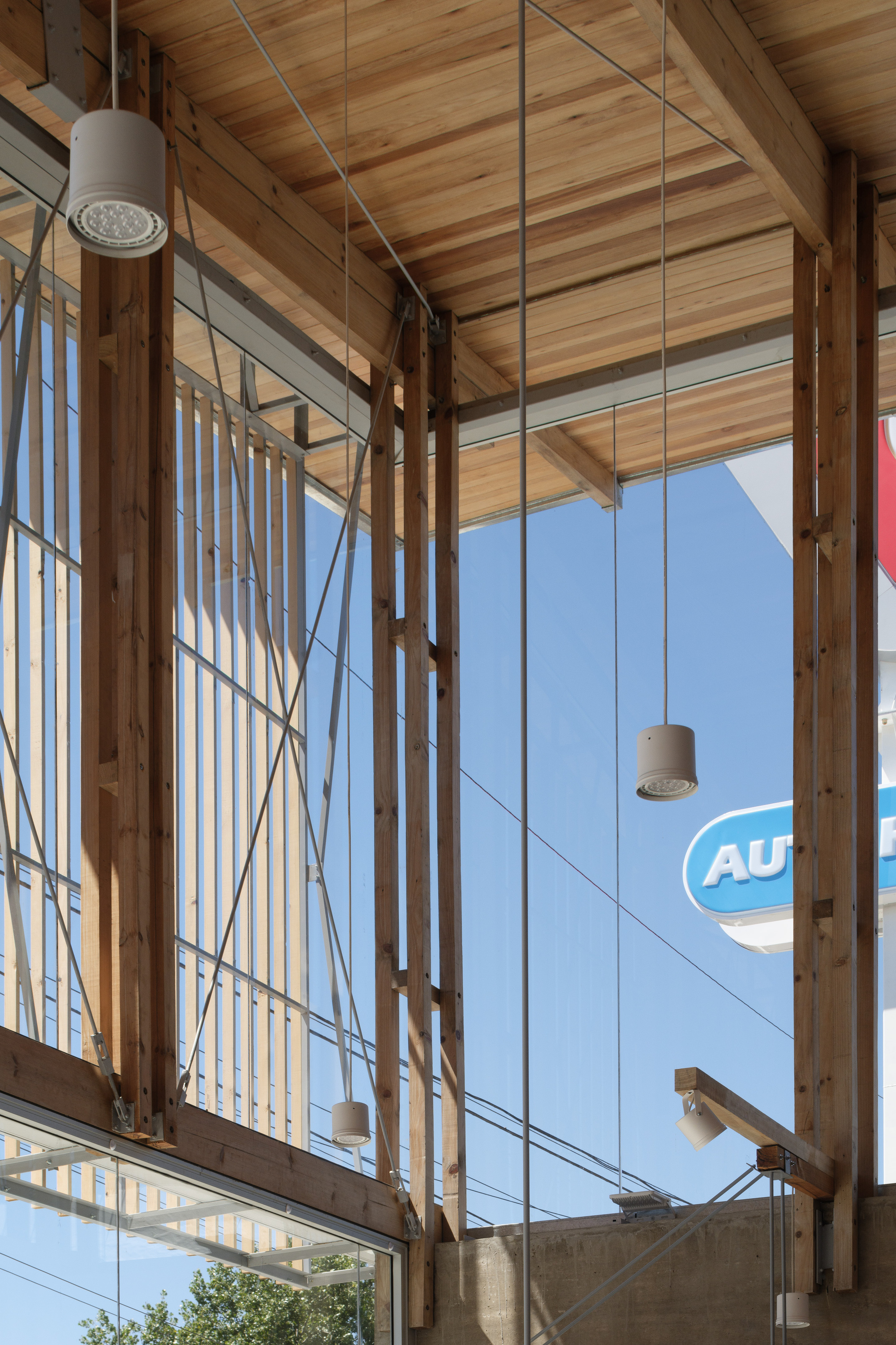 Close-up of paired timber posts, steel cable bracing and pendant lamps against glass and a blue sky