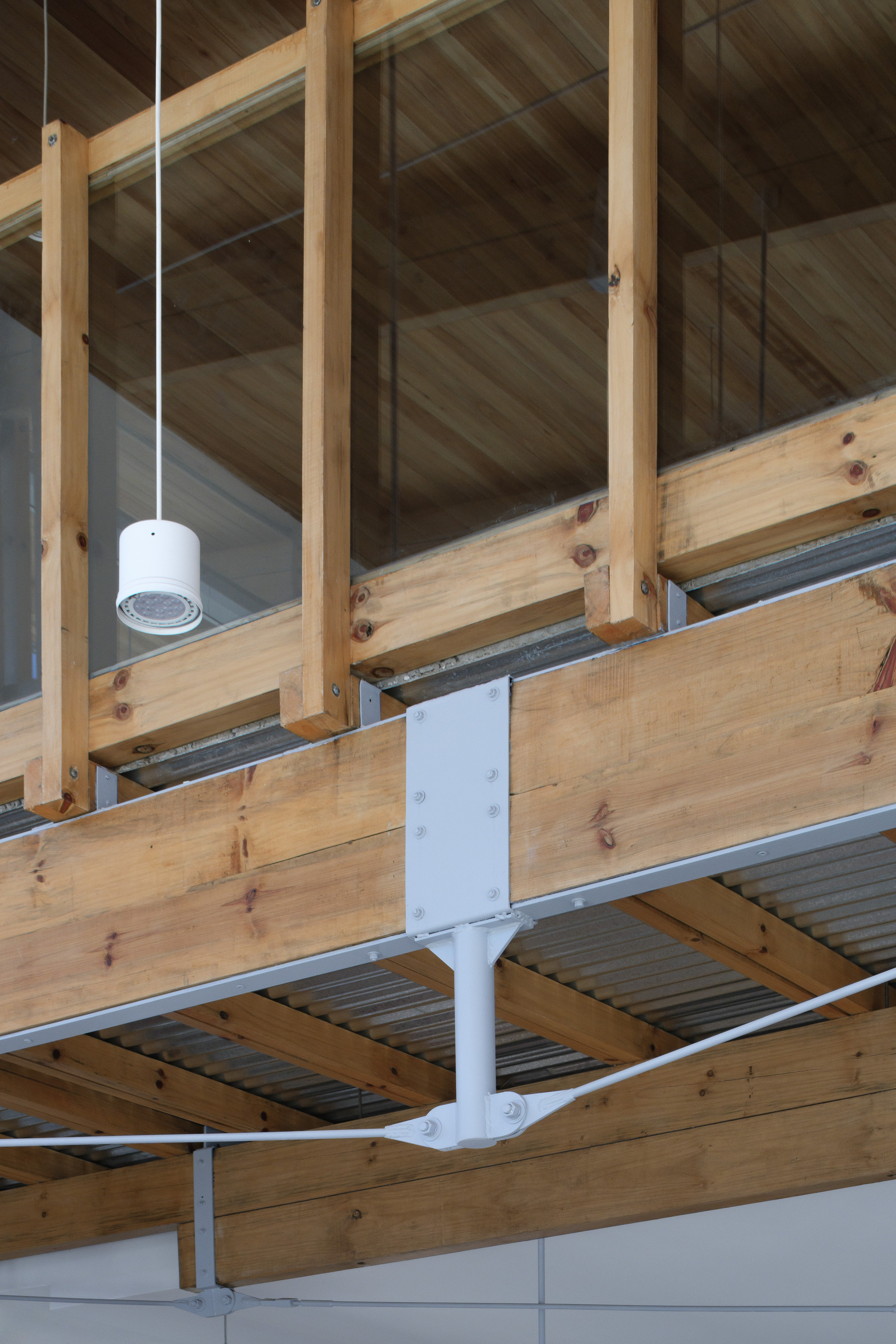 Detail of a timber beam bolted to a white steel plate, with a glass-backed wood balustrade above and a pendant lamp