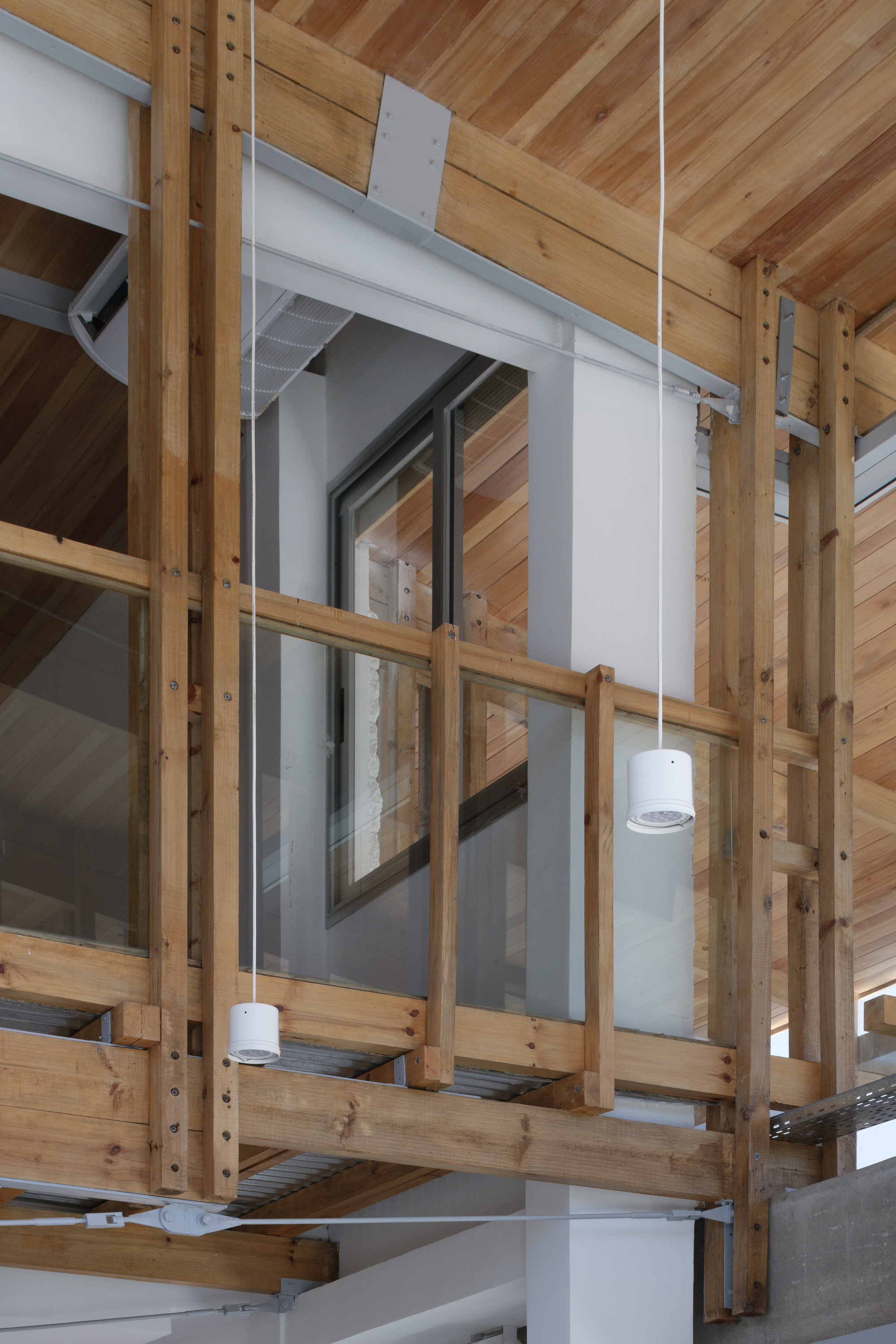 Upper-level timber framing with glass balustrade, a white column and a window opening, lit by hanging cylindrical lamps