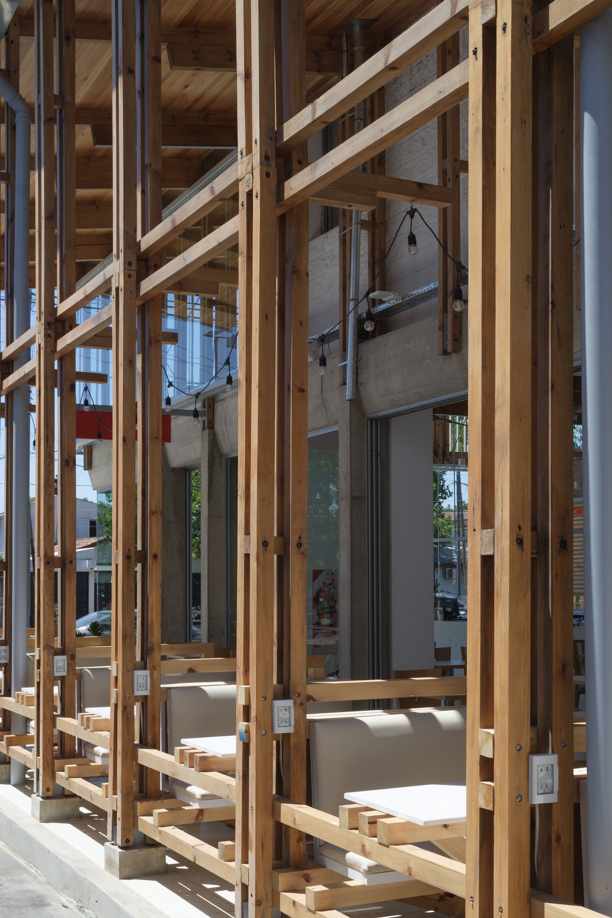 Timber post and beam screen along the cafe frontage, with fixed benches, string lights and bright afternoon sun