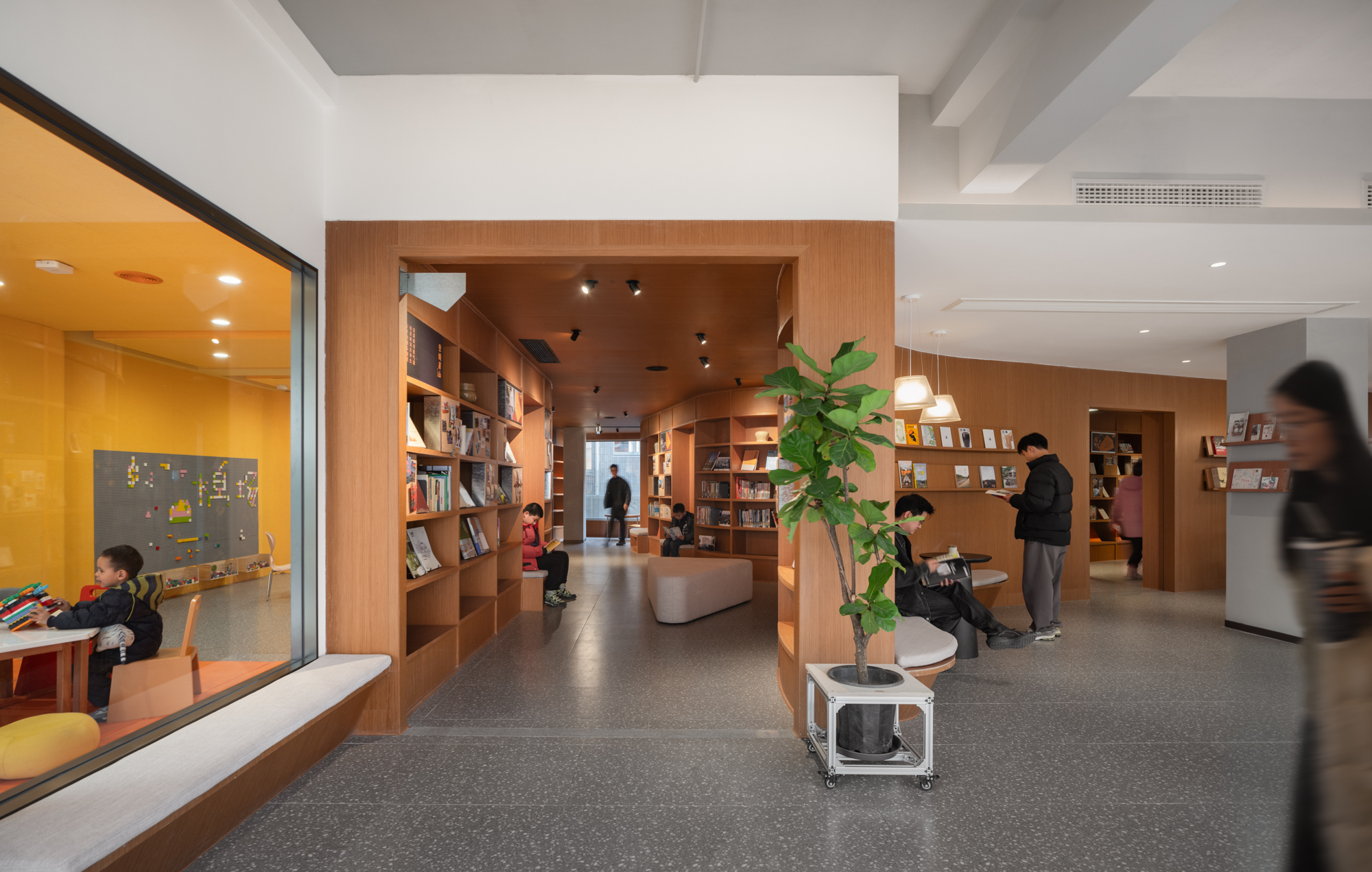 Timber-framed bookshelf alcoves opening off a terrazzo floor, with readers, a potted plant and a child in a window seat