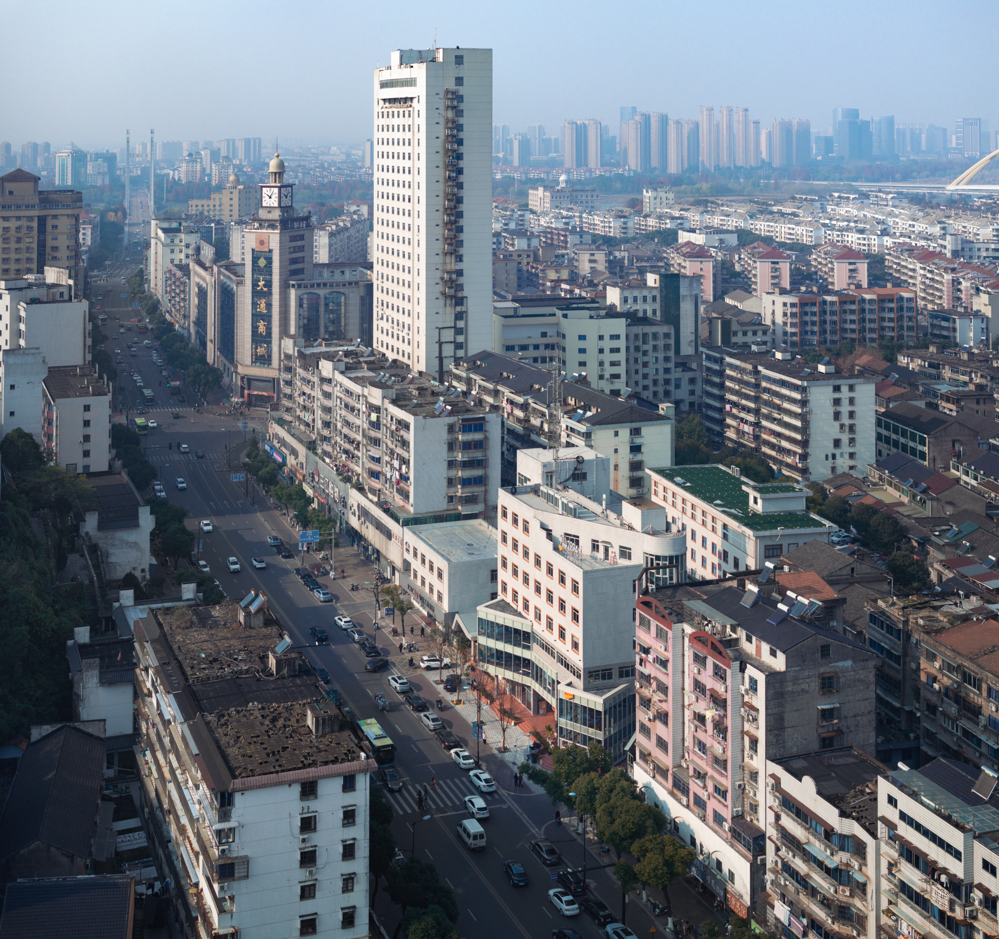 Aerial view down a wide avenue lined with mid-rise apartment blocks and a clock tower, under hazy morning light