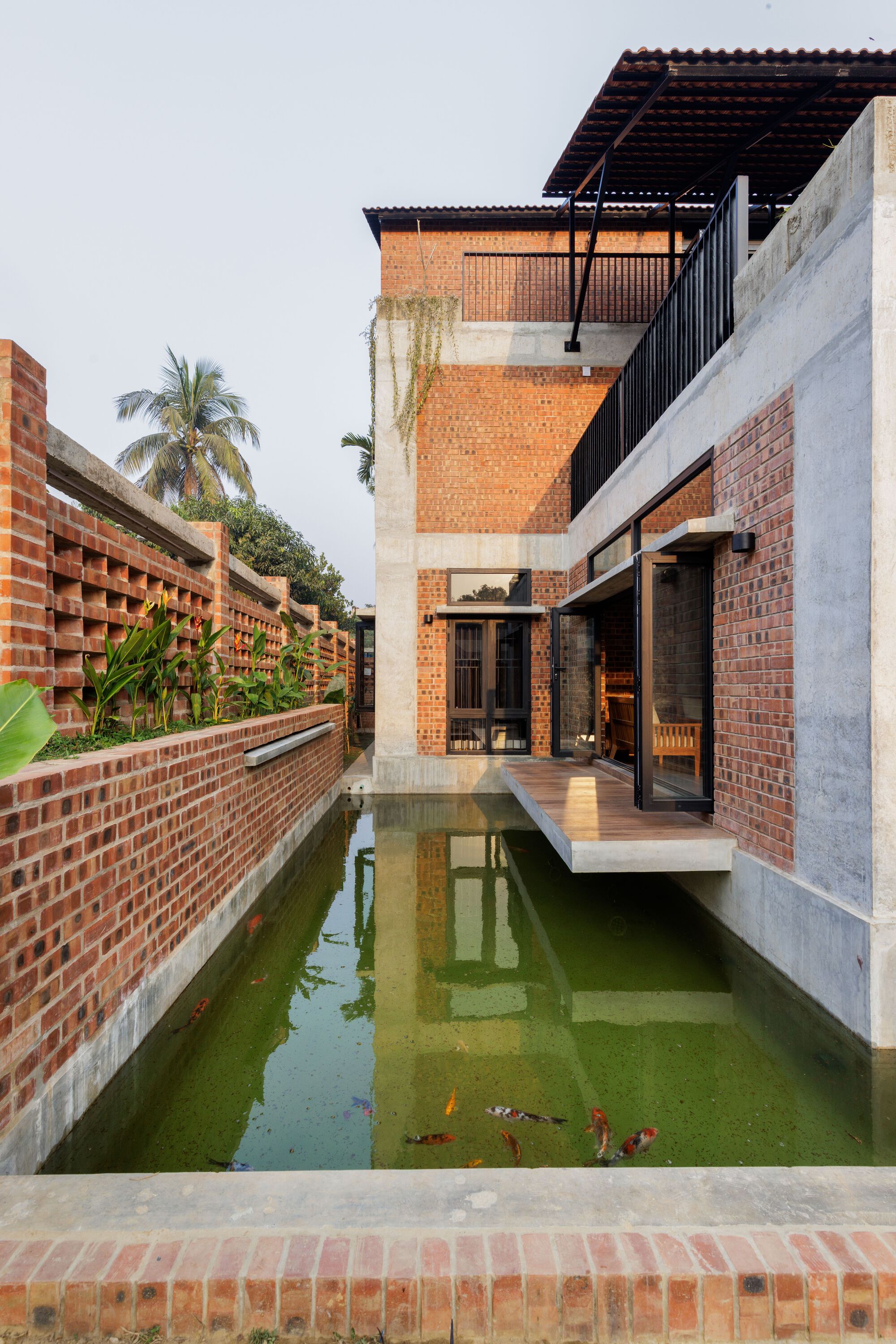 Brick and concrete house rising from a green koi pond, with a timber deck projecting over the water