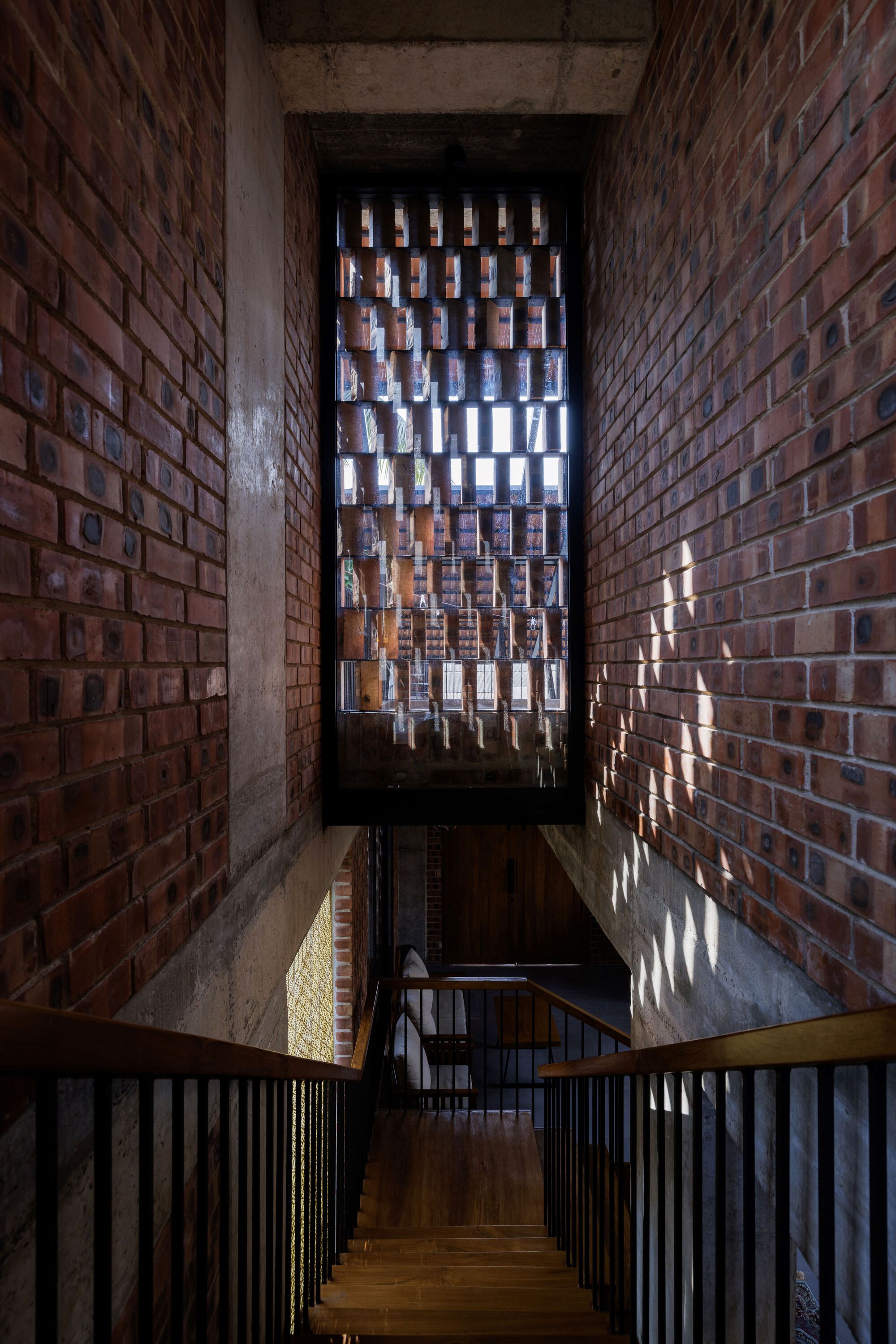 Brick-lined stairwell with a perforated brick screen at the top, sunlight dappling the walls above timber treads and steel balustrades
