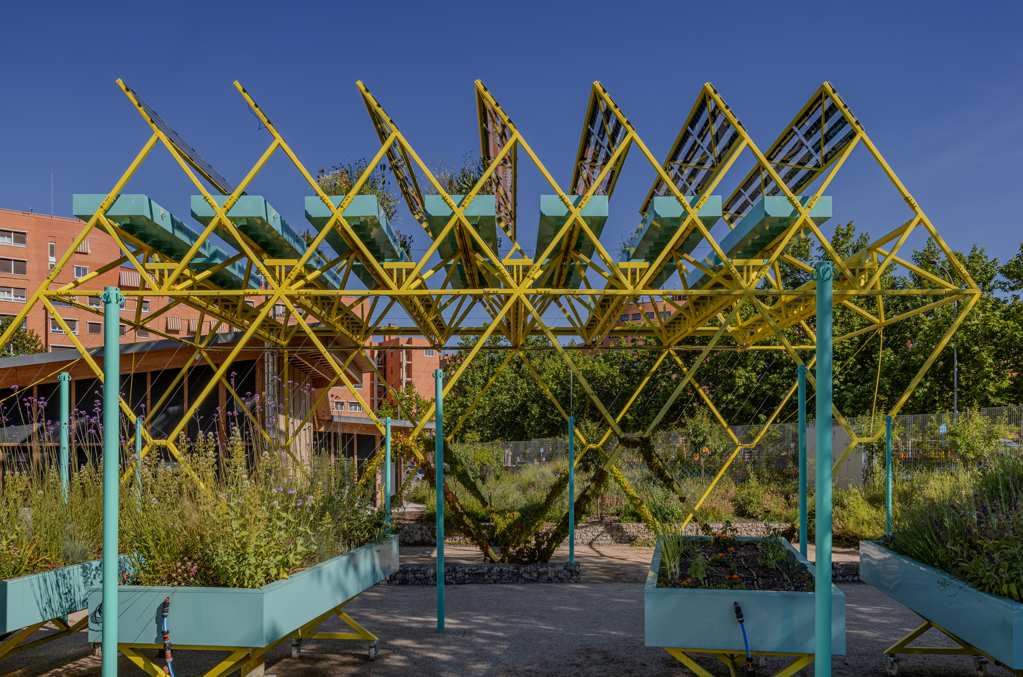 Zigzag yellow steel frame with tilted solar panels above teal planter boxes and green posts under a deep blue sky