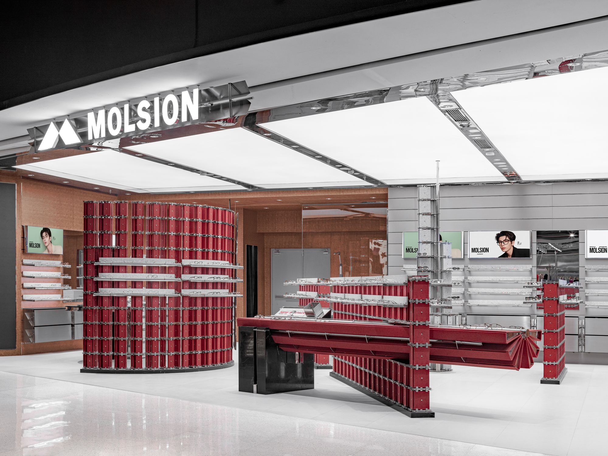 Store entrance with a backlit white ceiling grid, a cylindrical red display tower and a fan-folded red counter on a glossy floor