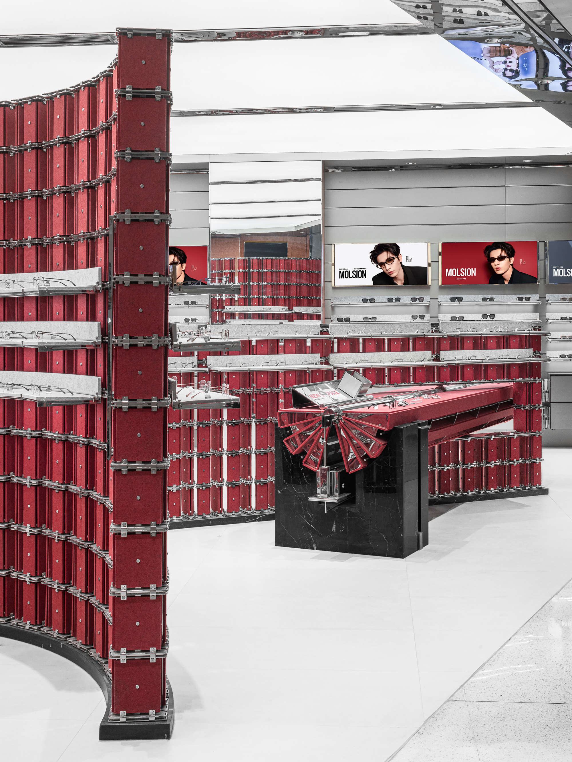 Curved red display wall in the foreground, with a black stone plinth and fan-pleated red counter beyond, beneath portrait screens