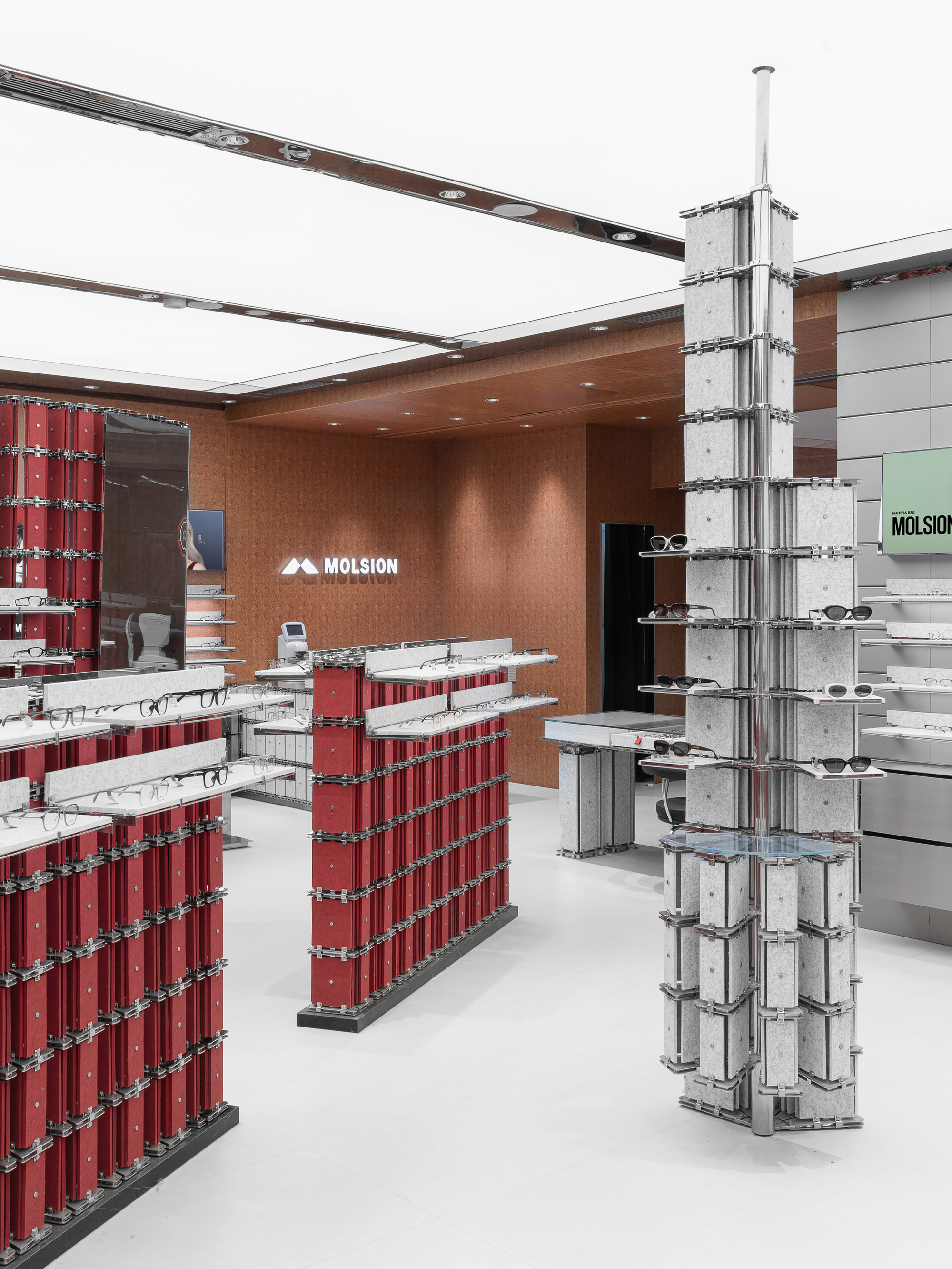 Eyewear store interior with a freestanding red display unit, a grey felt column of sunglasses shelves and a luminous white ceiling