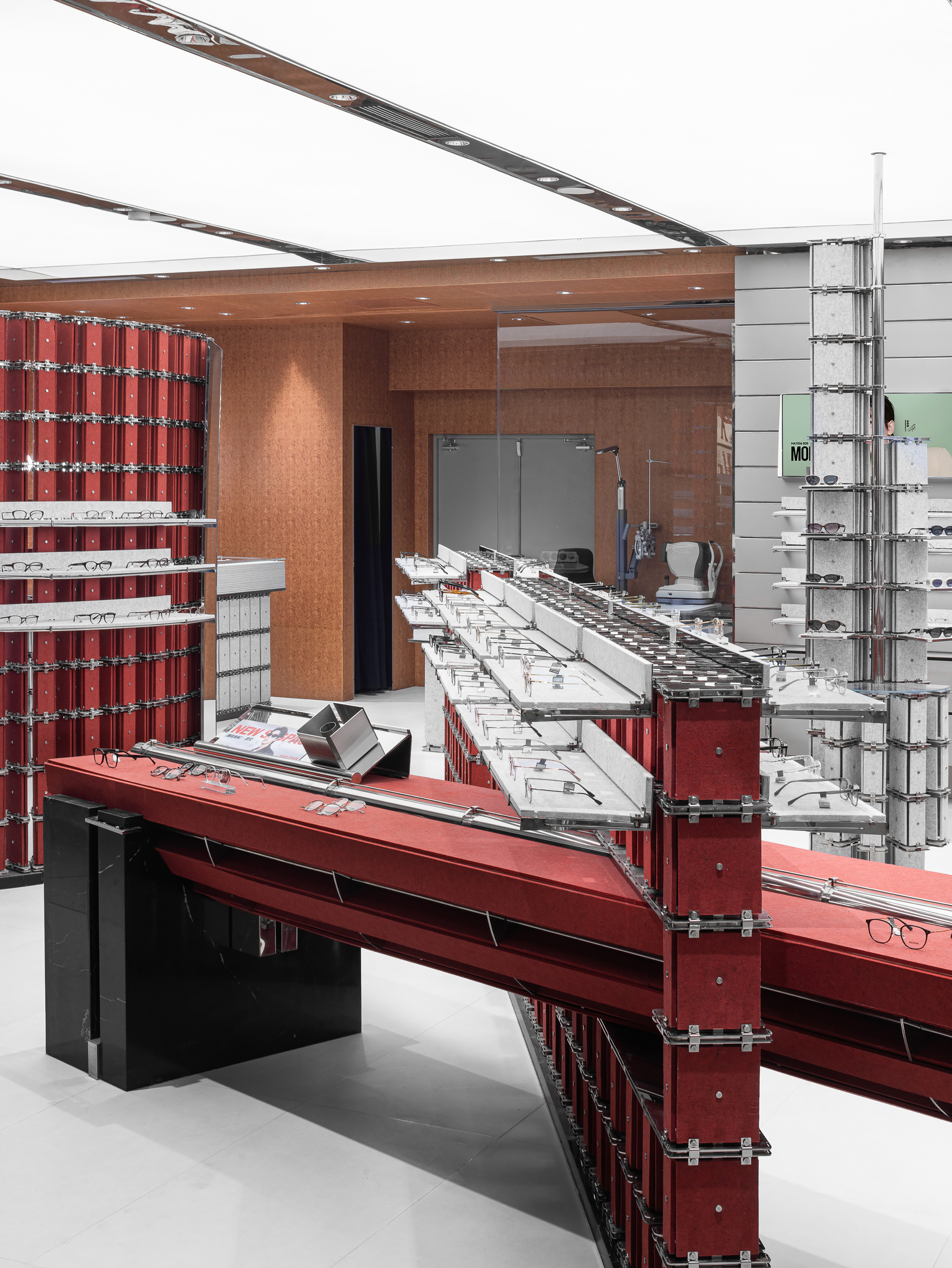 Red felt display table on a black stone base, cantilevering toward angled glasses shelves and a curved red wall behind