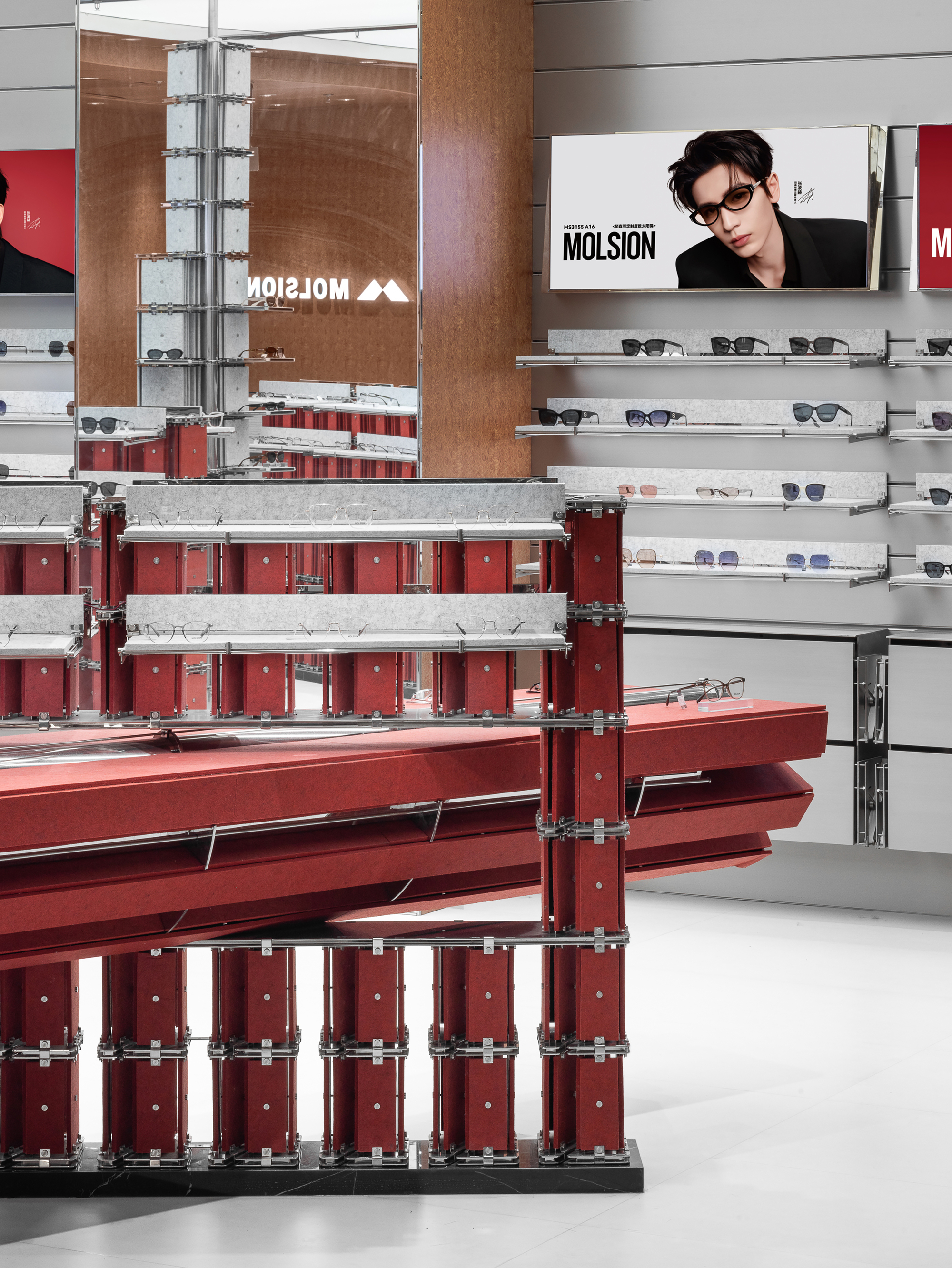 Red felt display frame with grey shelves of glasses, set against a wall of sunglasses and a portrait advertisement