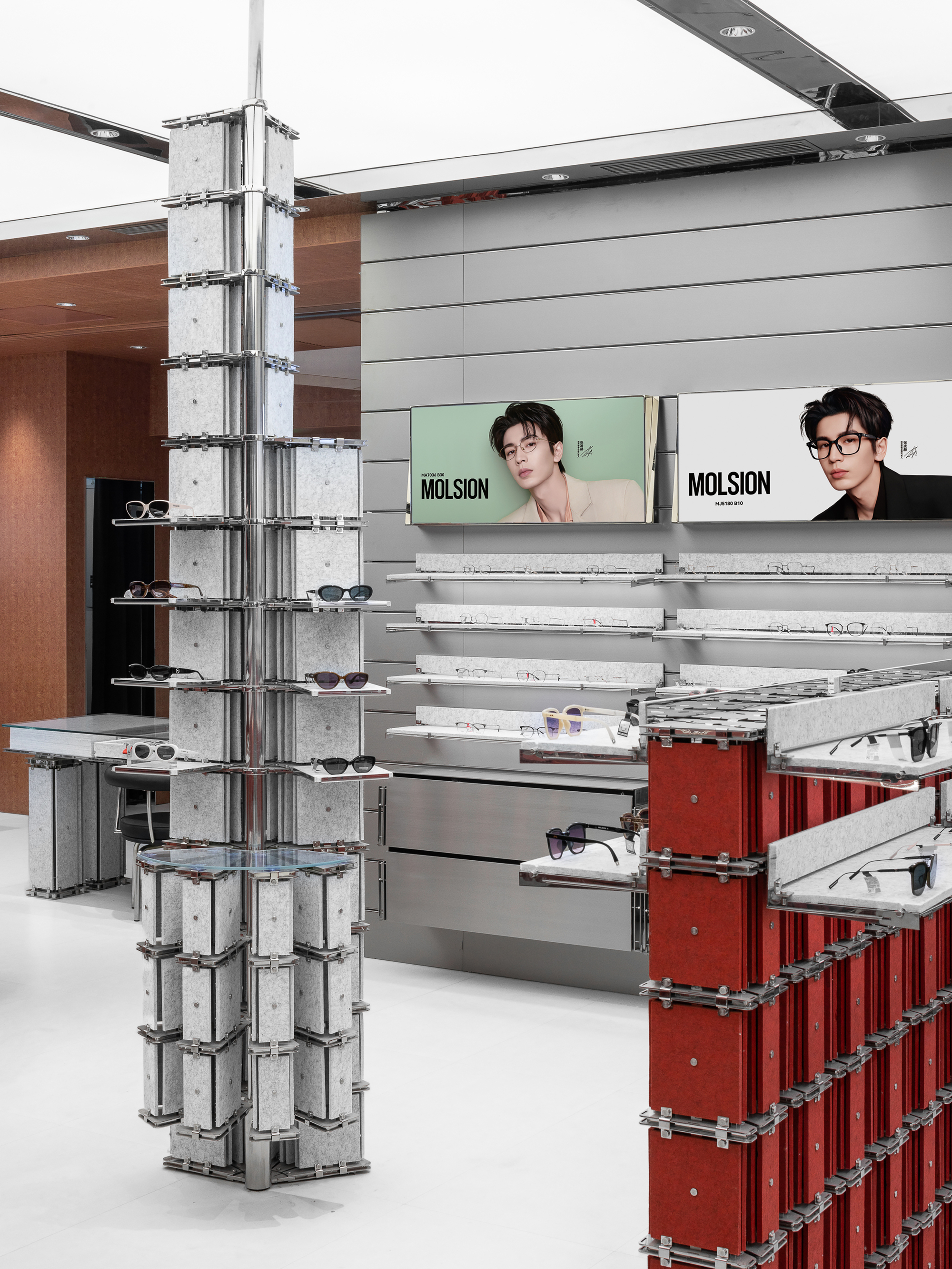 Grey felt-panel display column with steel clamps beside a red stacked display unit, under a glowing white ceiling