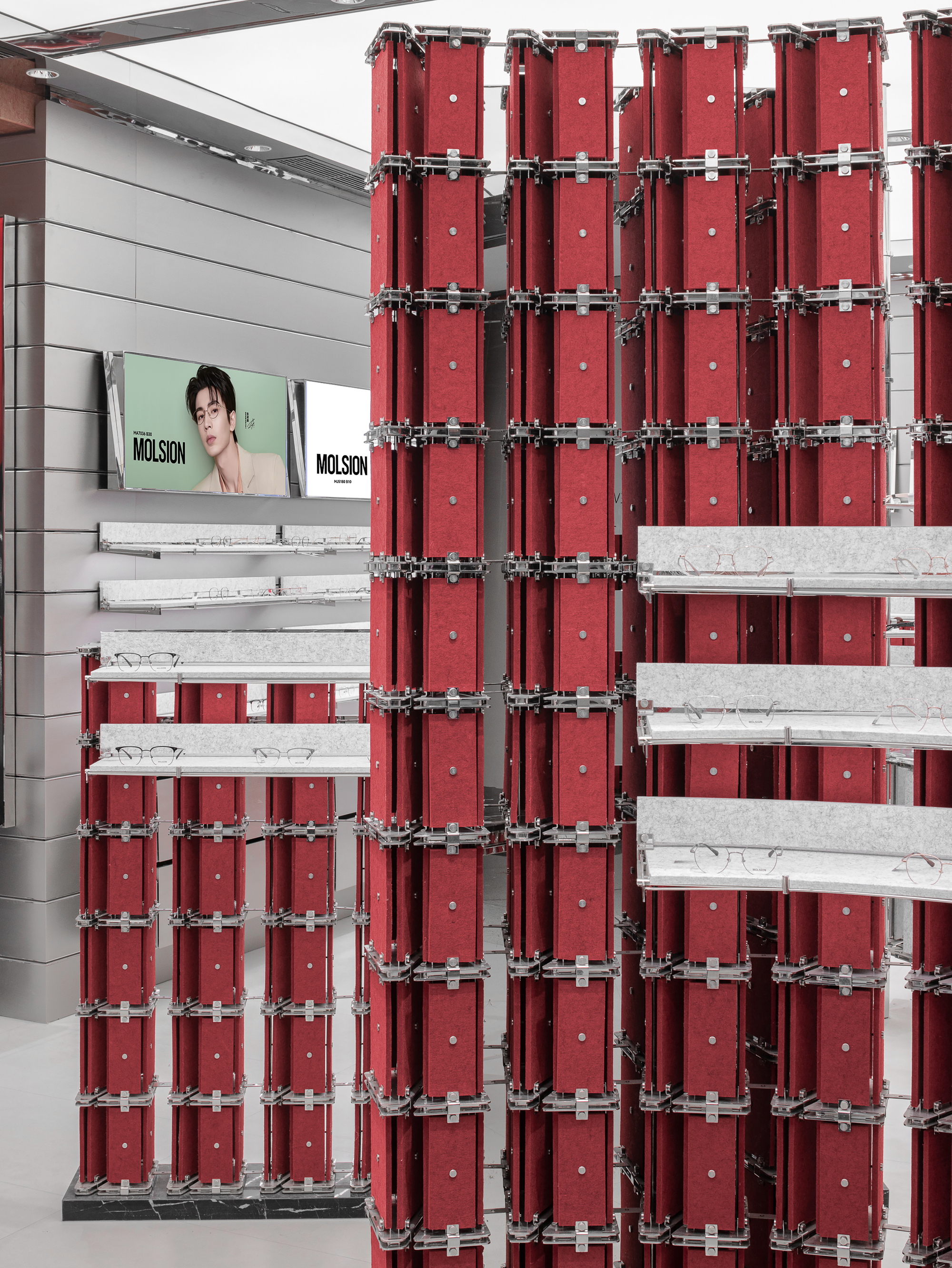 Close-up of stacked red felt panels joined by steel clamps, with glasses resting on pale speckled shelves