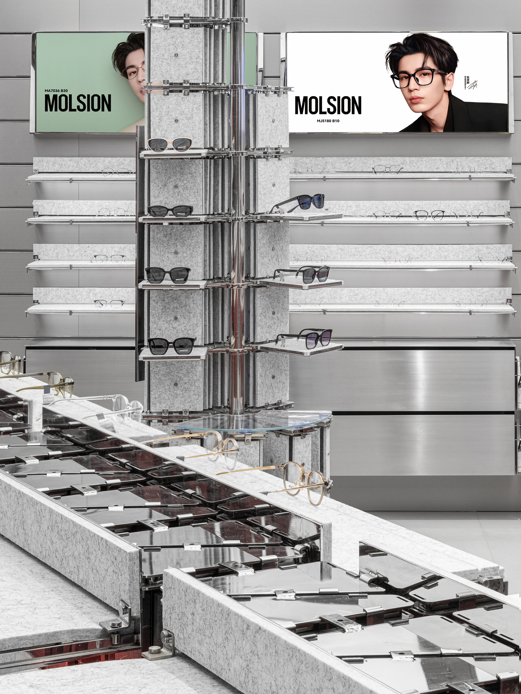 Felt-topped display counter with mirrored steel trays and round gold frames, a sunglasses tower and wall shelves behind under bright light