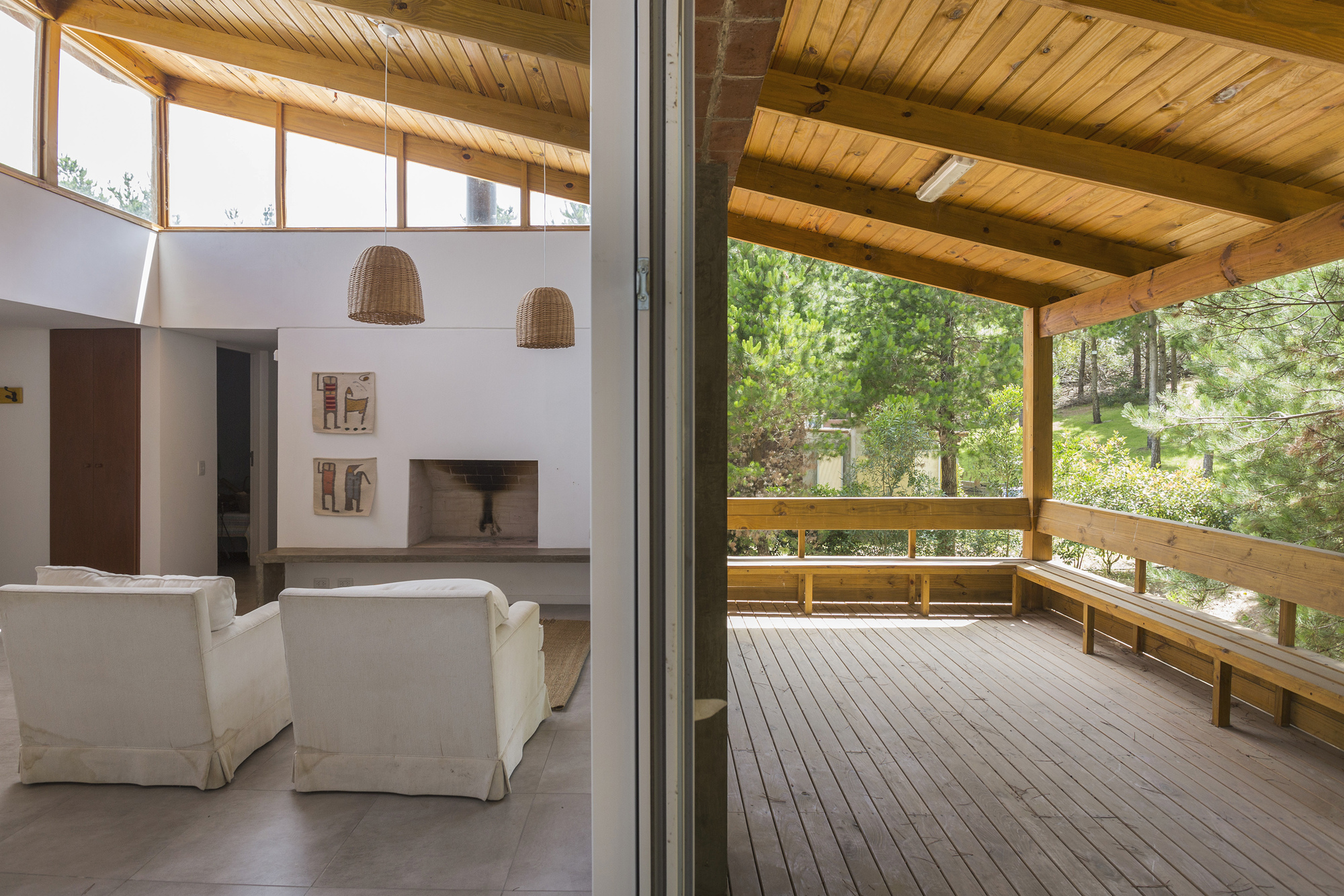 View from the living room through a sliding door to a timber deck porch with built-in bench among pines