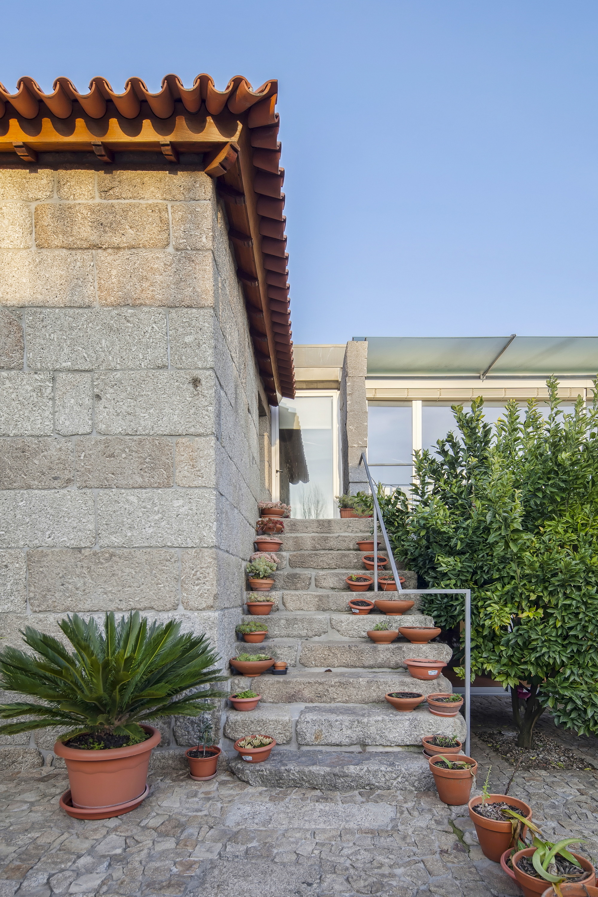 Granite steps lined with small terracotta pots rising beside a stone wall under a clear blue sky
