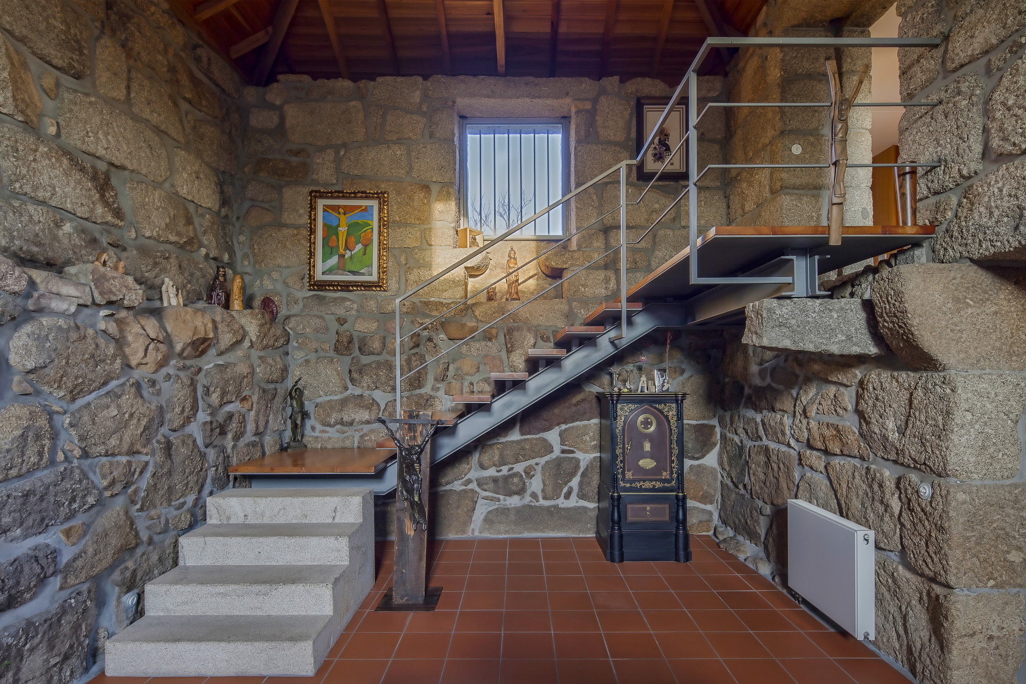 Wide view of the stone room with a suspended steel stair, granite steps and a radiator against the wall