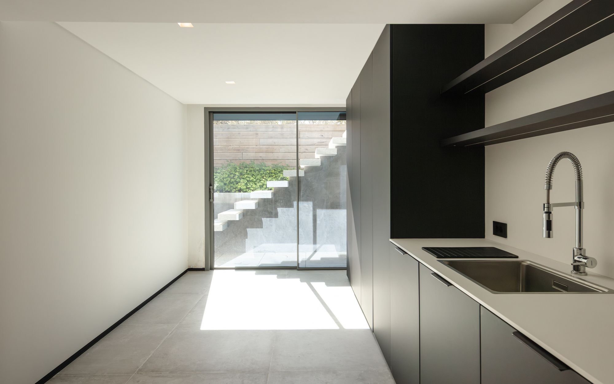 Lower-level kitchen with black cabinets and steel tap, a sliding glass door framing a white stair outside in a patch of sunlight