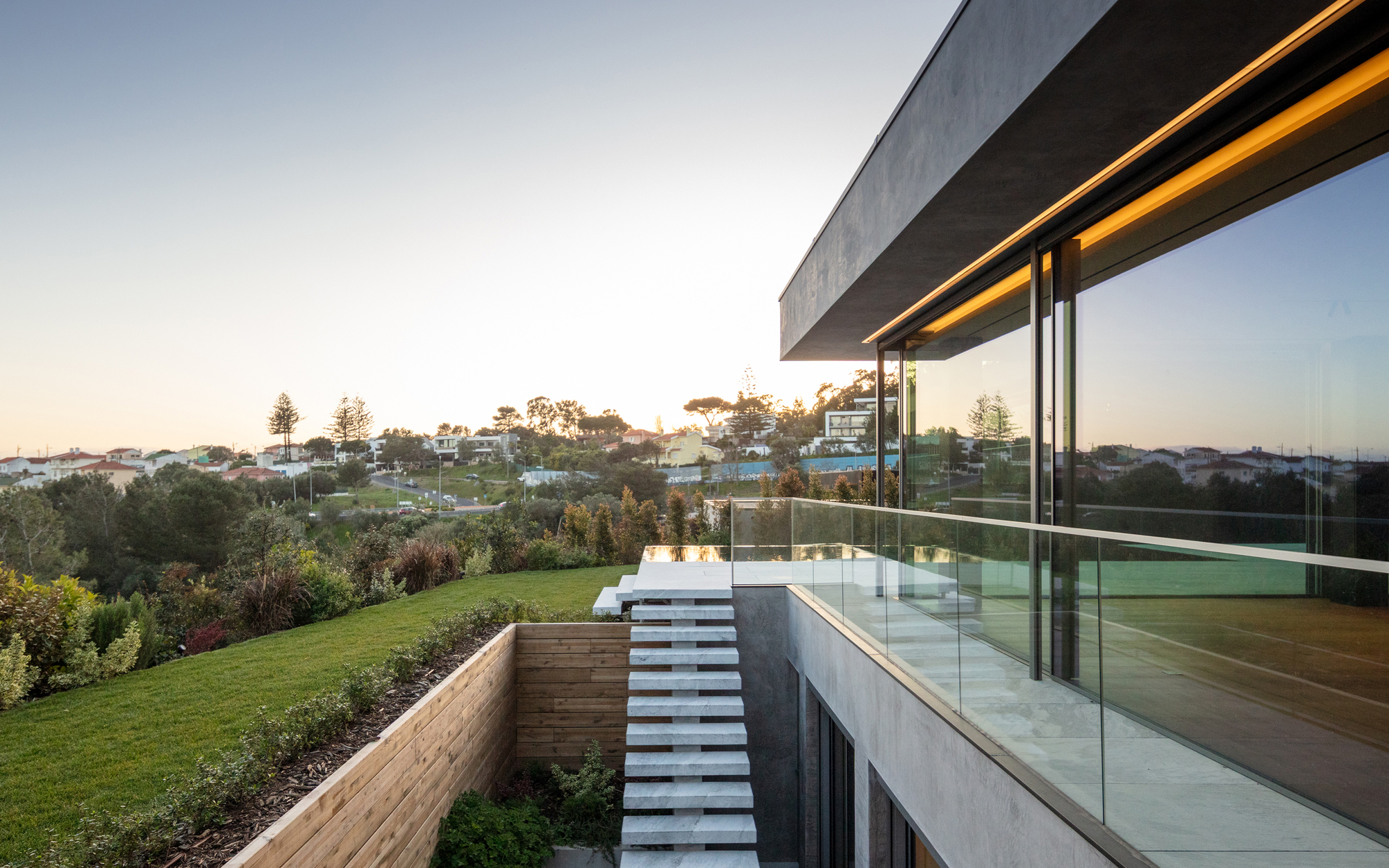 White stone steps descending beside a timber retaining wall and glass balustrade, with hillside houses in the dusk haze