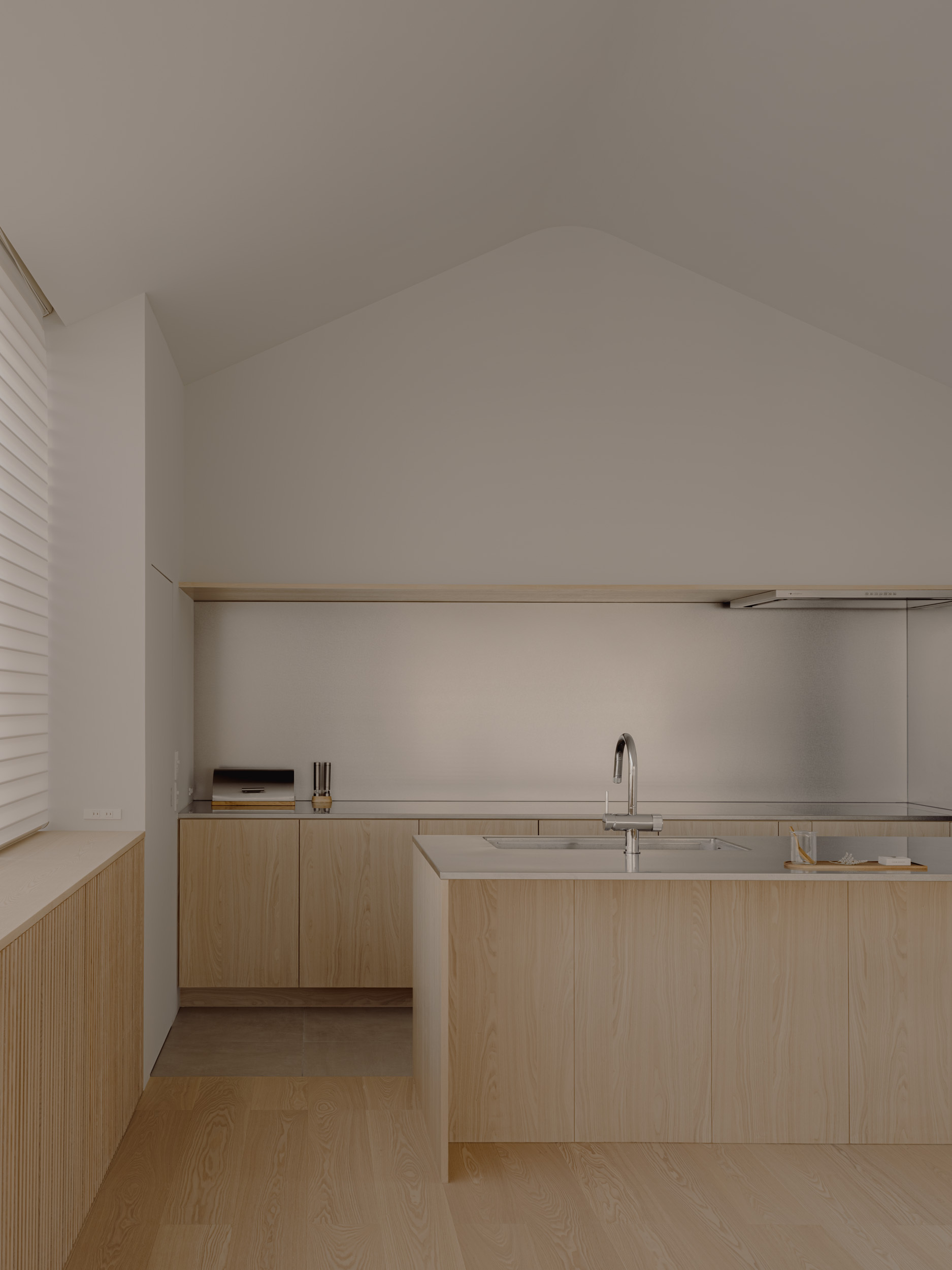 Kitchen with pale oak cabinetry, a steel backsplash and an island under a pitched white ceiling in soft light