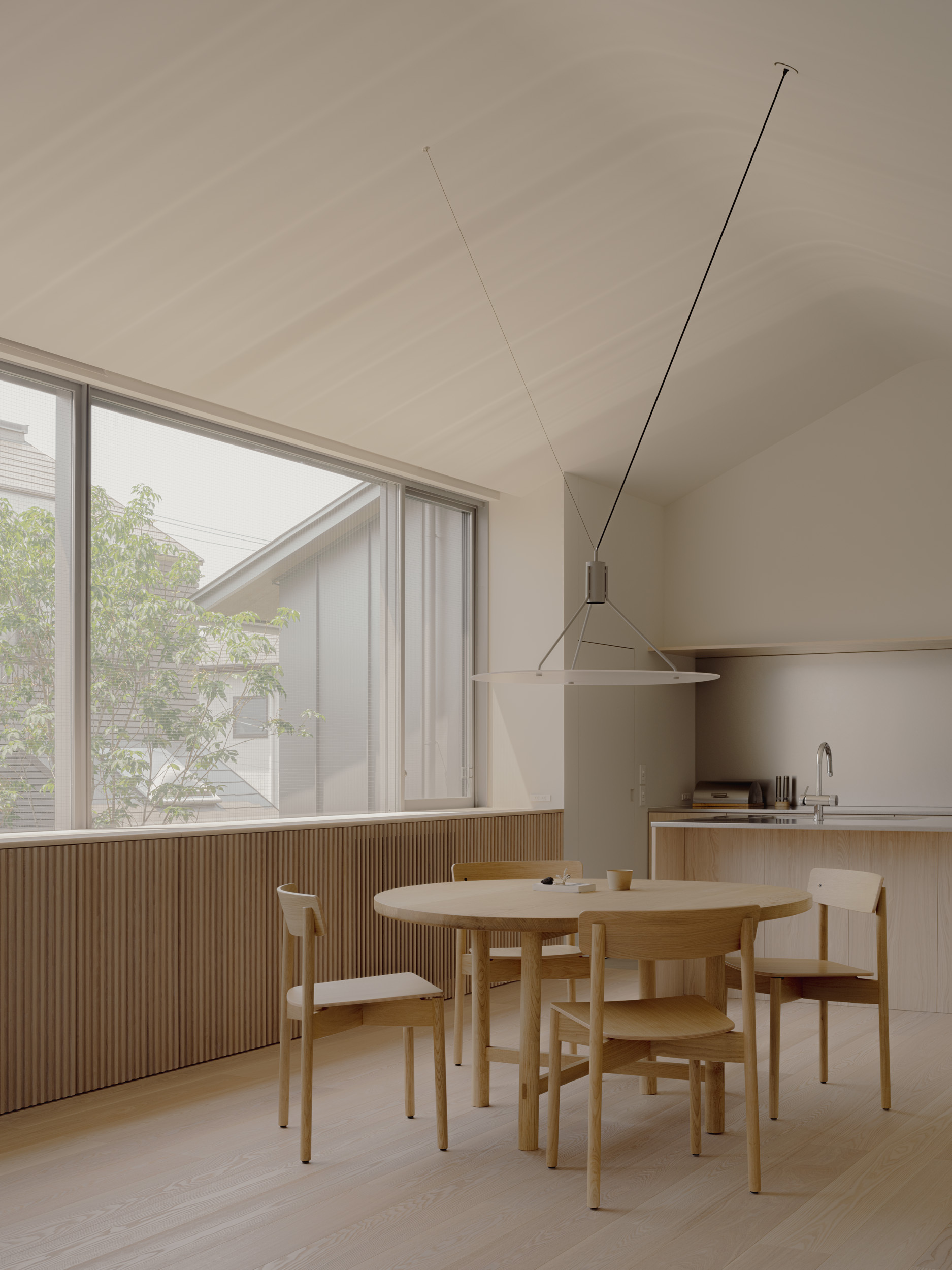 Dining area with round oak table, slatted timber wall panelling and a vaulted ceiling beside a large window in soft daylight