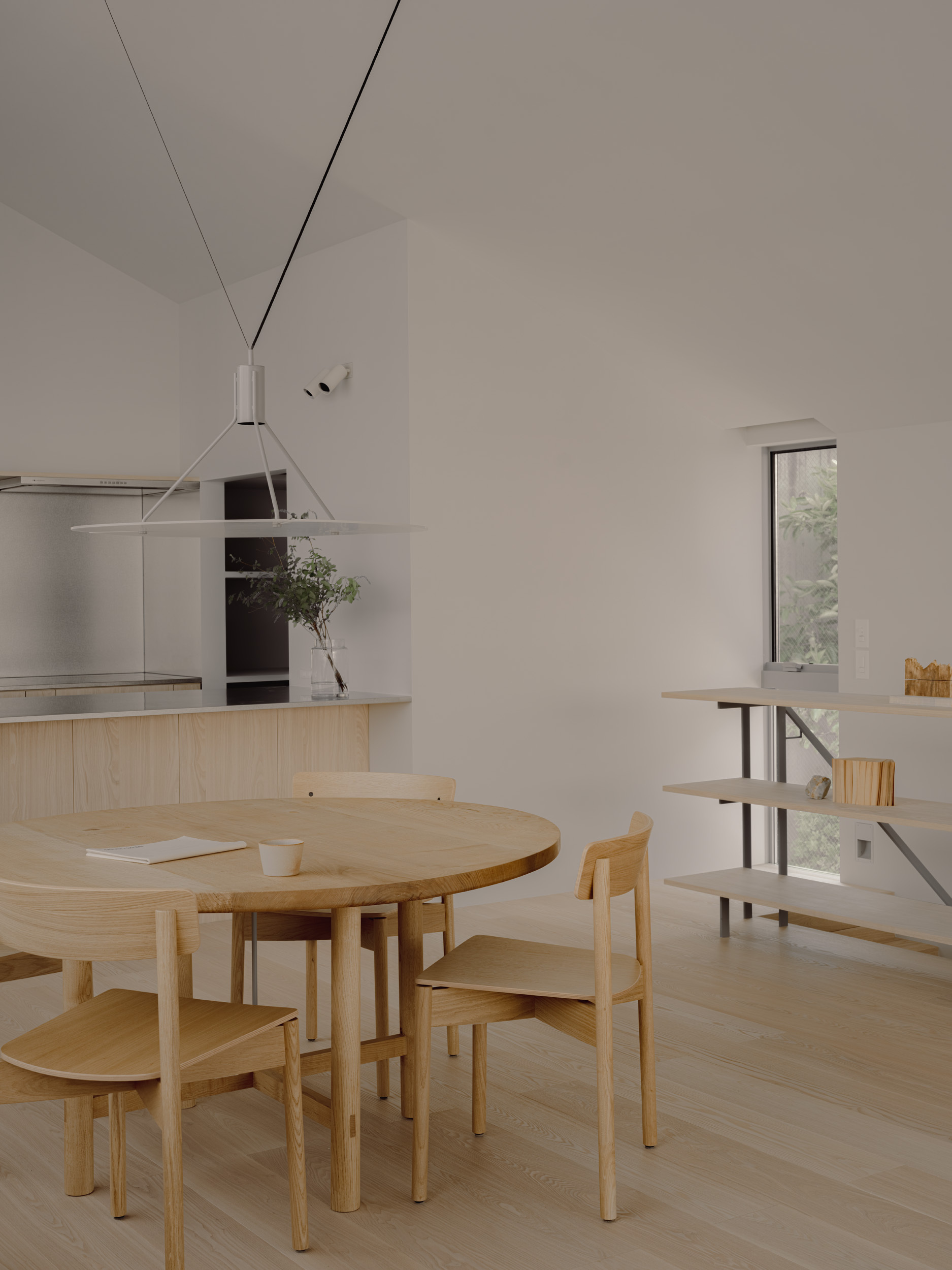 Round oak dining table and chairs below a pendant lamp, with open shelving and a narrow window onto greenery