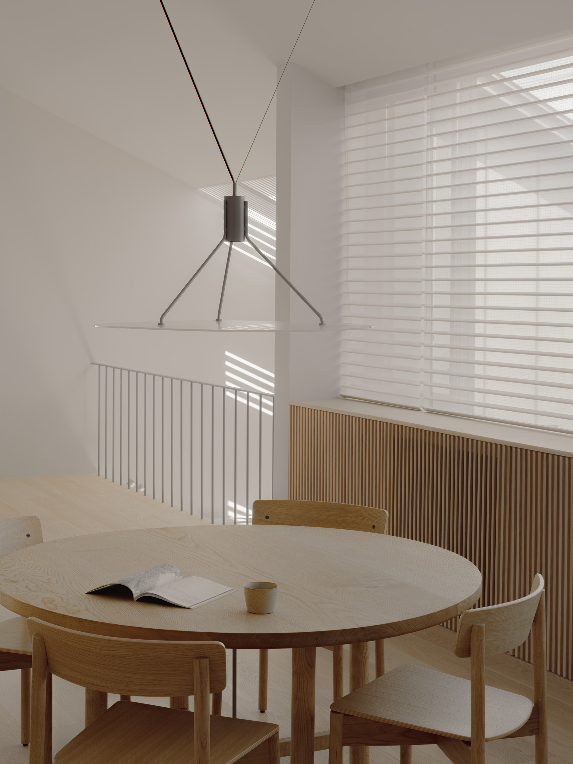 Pendant lamp hanging above a round table, with striped sunlight through sheer blinds and a slim metal stair railing behind
