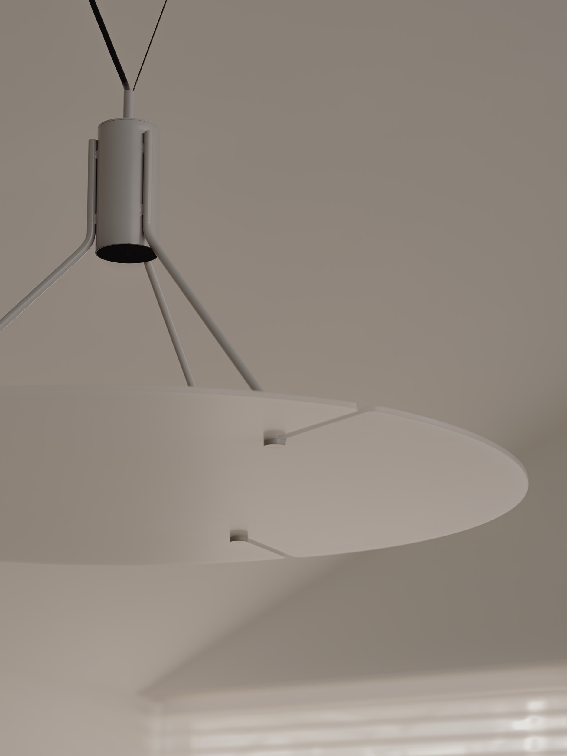 Close-up of a pale disc pendant lamp hung from thin black cables, its slender legs meeting a cylindrical canopy in soft daylight