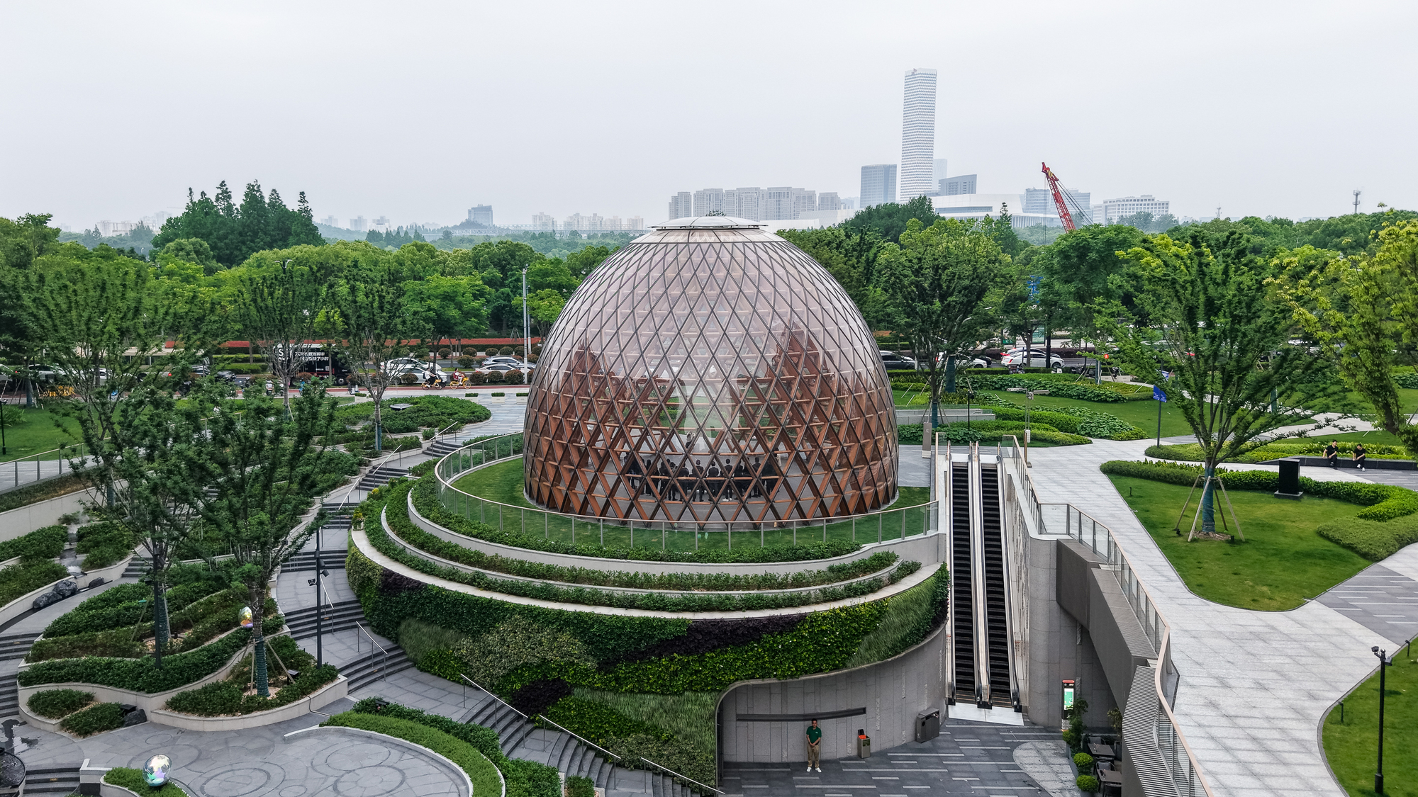 Elevated view of the lattice dome ringed by green terraces, stairs and an escalator on a hazy day