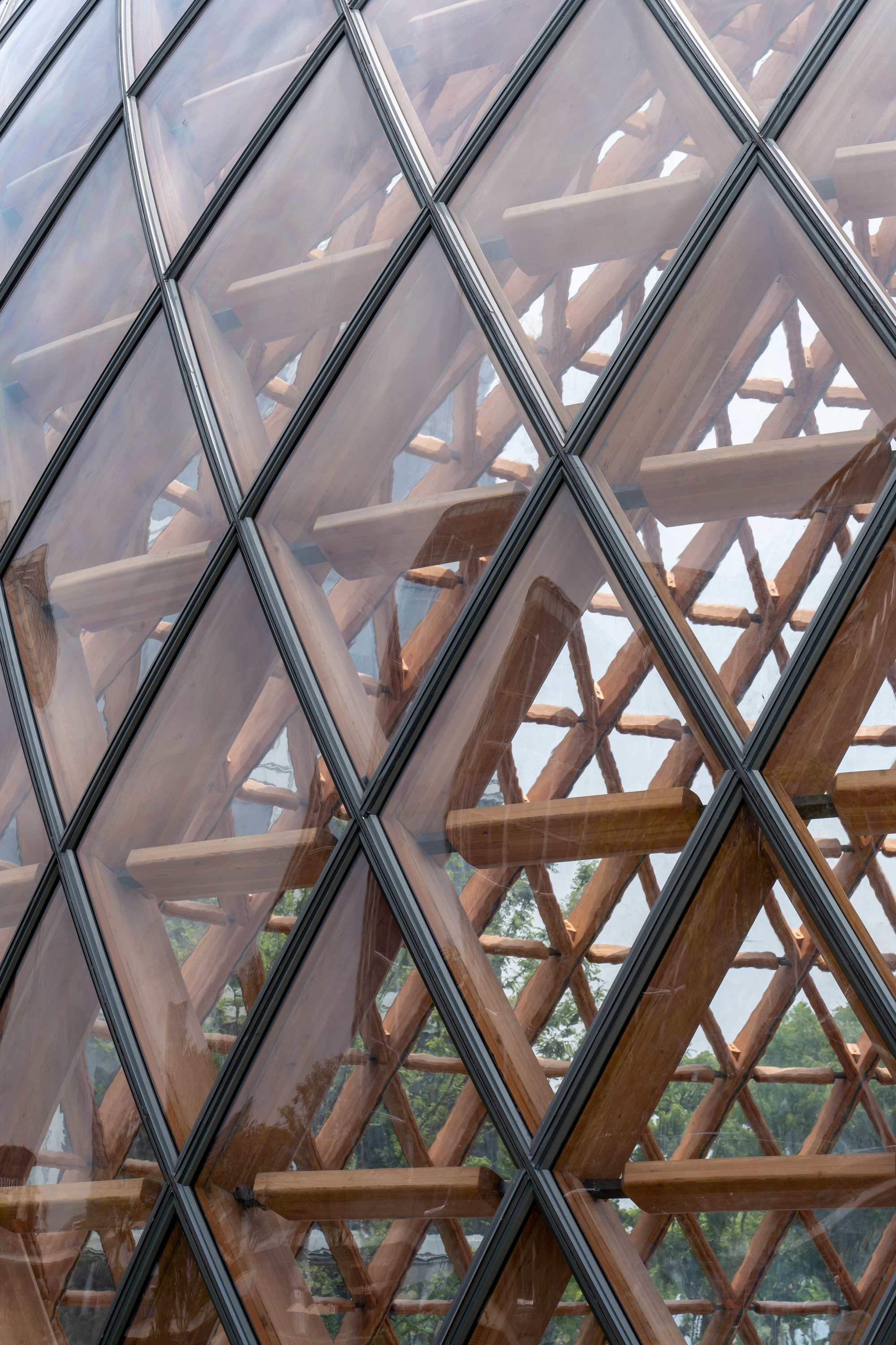 Close-up of glazed diamond panels over a timber lattice with horizontal wooden bars, trees blurred behind in soft daylight
