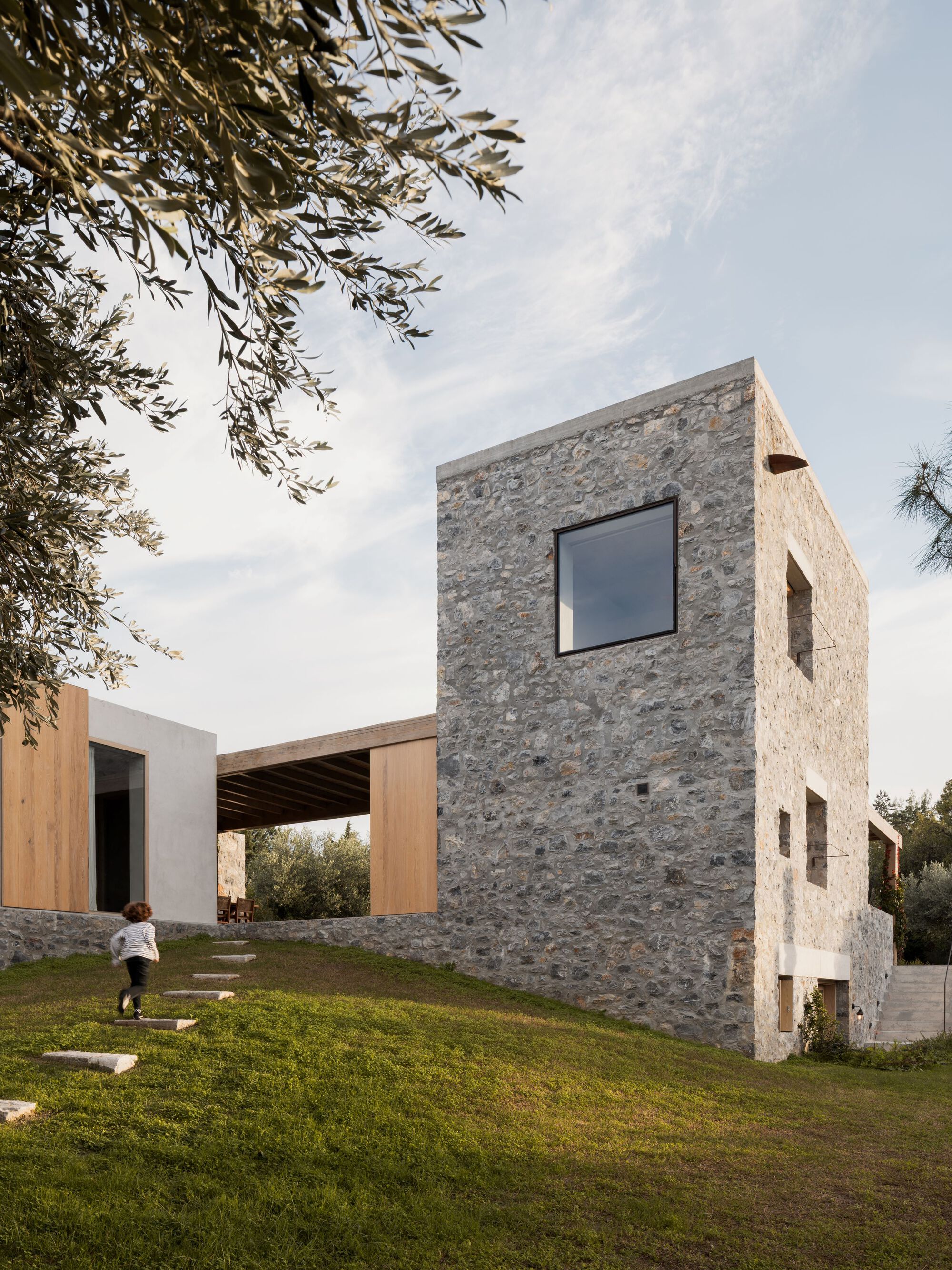 Rubble stone tower with a square black-framed window, and a child running up a grass slope past stepping stones