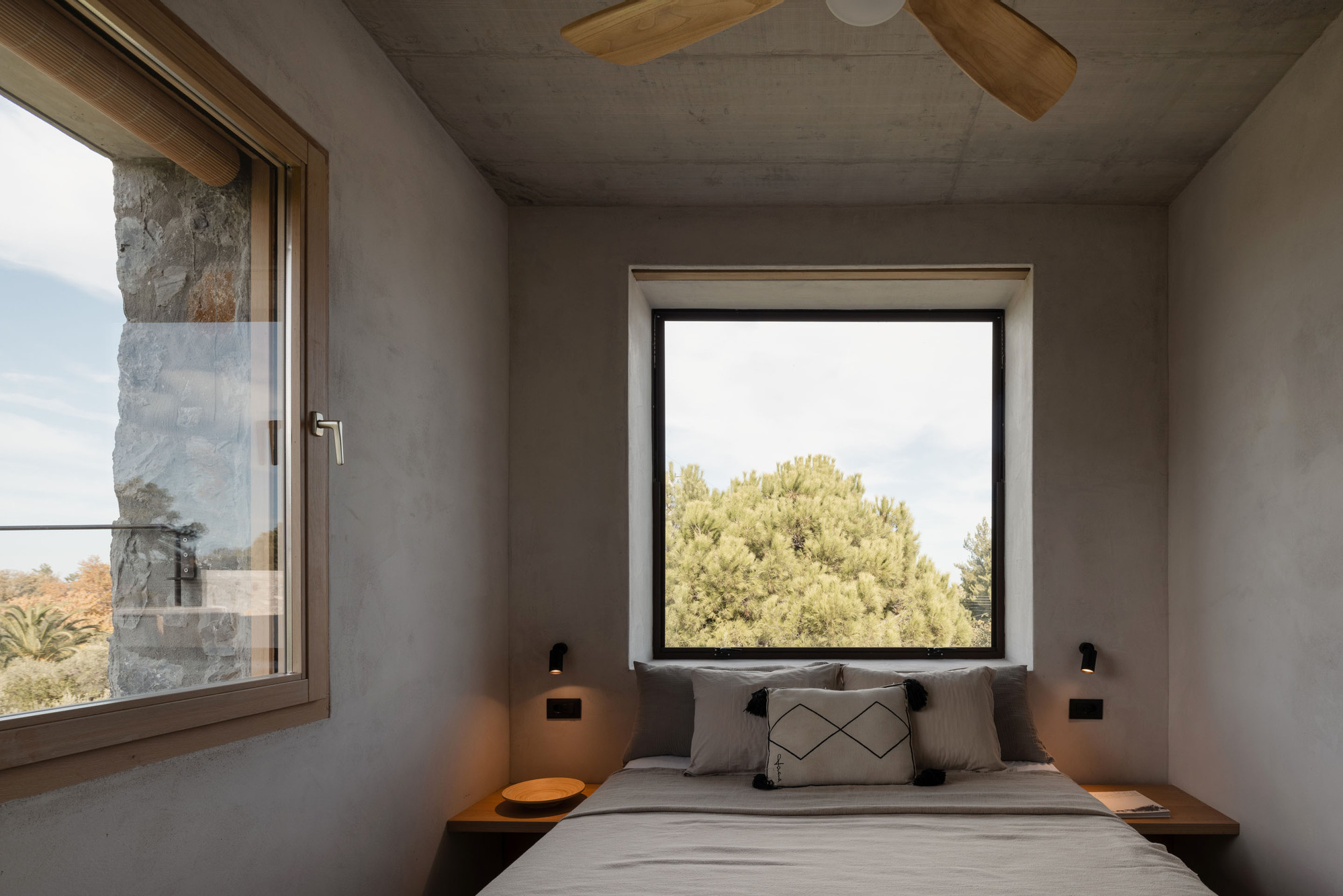 Bedroom with a square black-framed window above the bed, a ceiling fan and a timber-framed side window