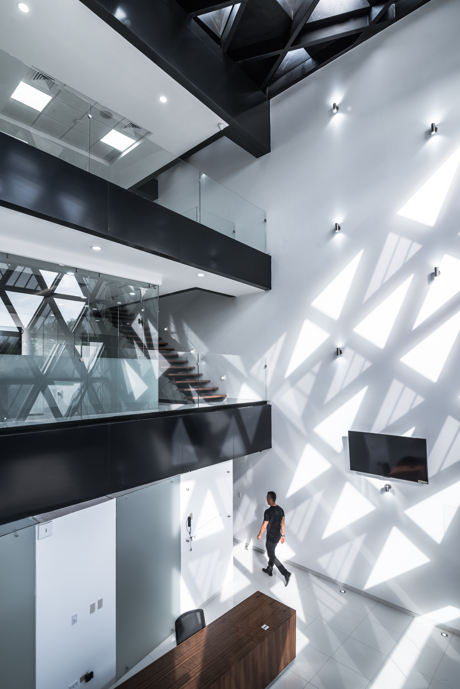 Lobby seen from above, with black balcony edges, a wooden desk and sharp triangles of sunlight on the wall