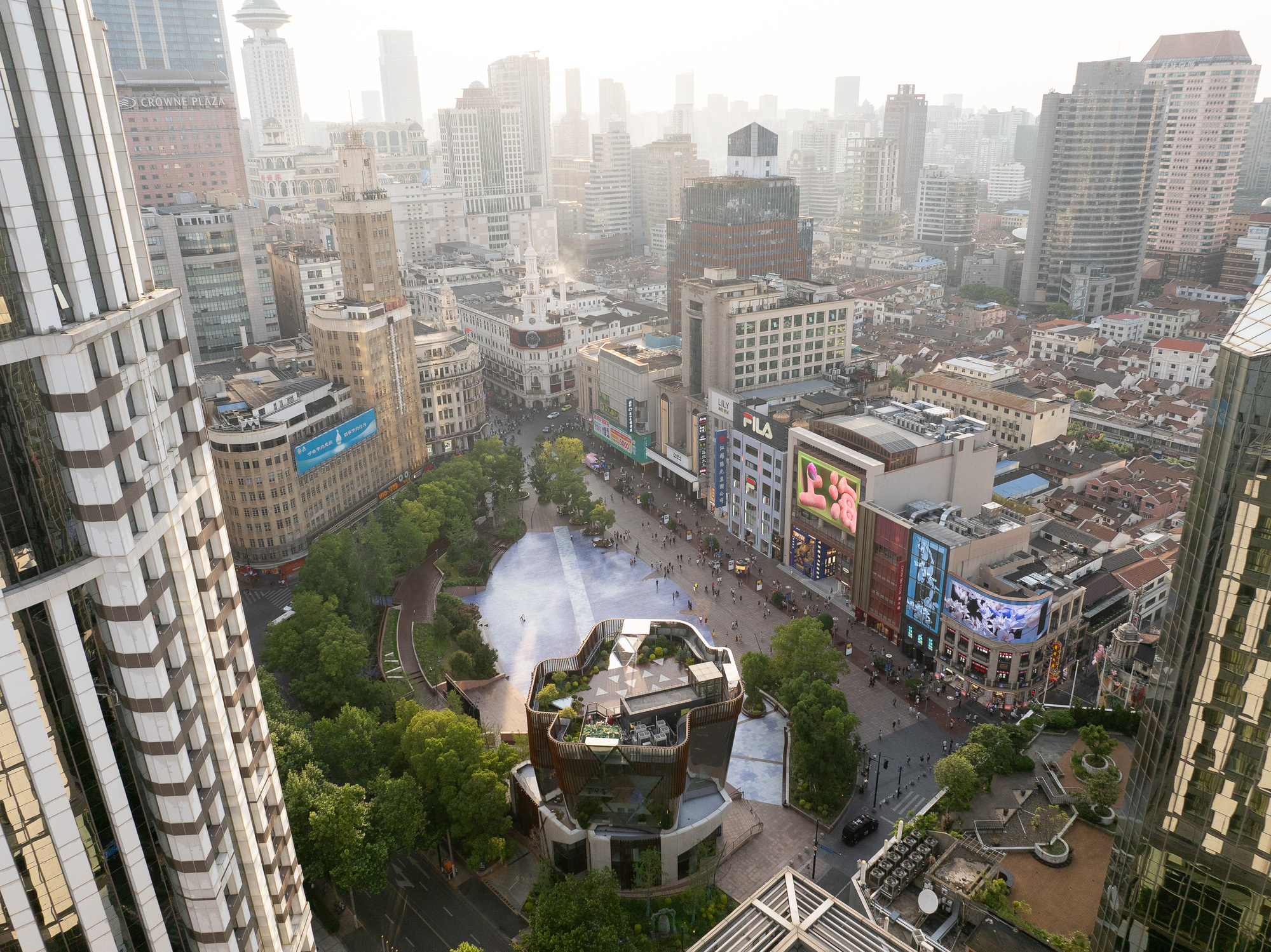 Aerial view of the plaza and the planted rooftop of the pavilion, surrounded by towers in morning haze