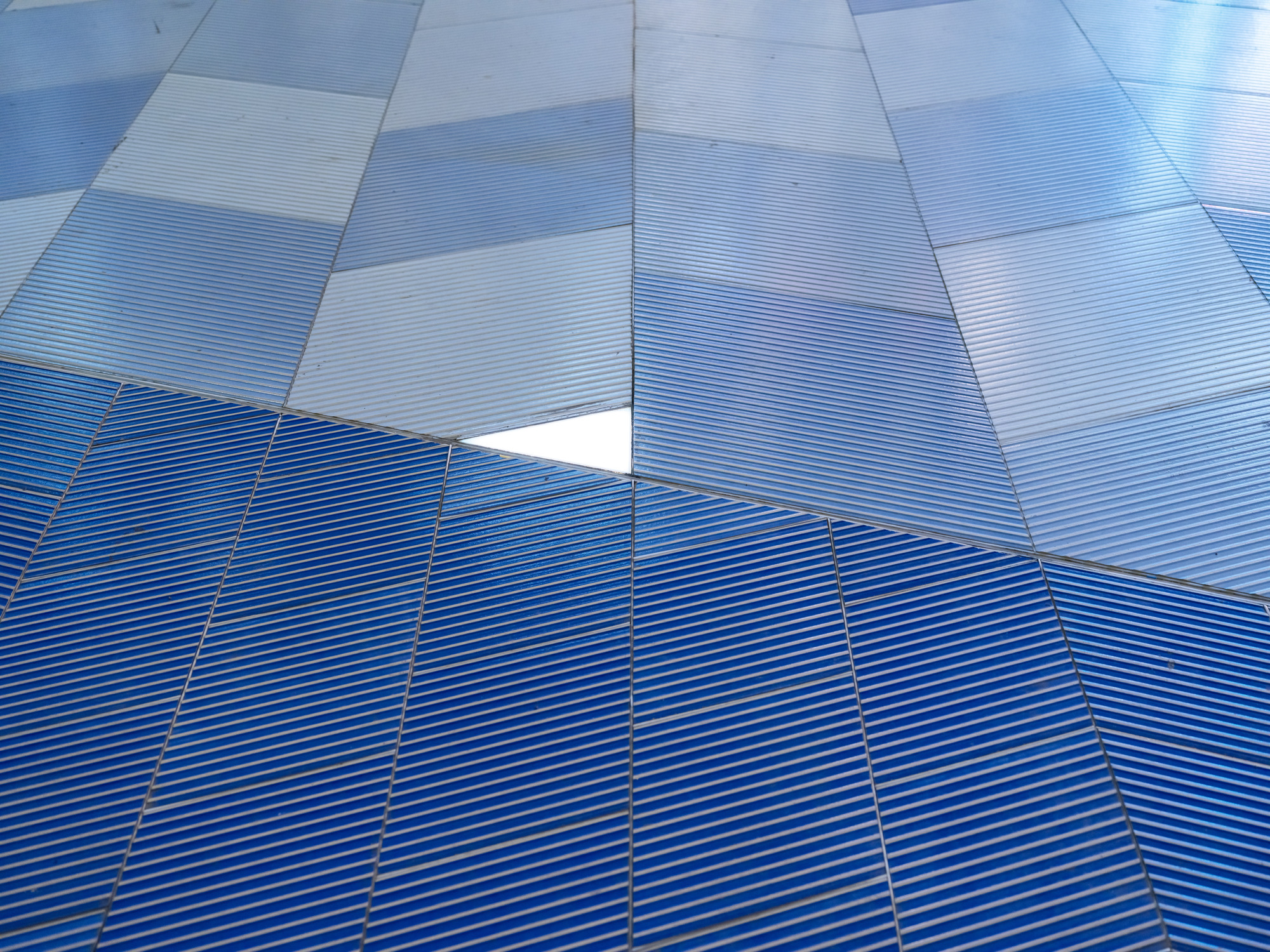 Close-up of ribbed blue paving tiles shifting from deep blue to pale blue, with a small gap showing white beneath