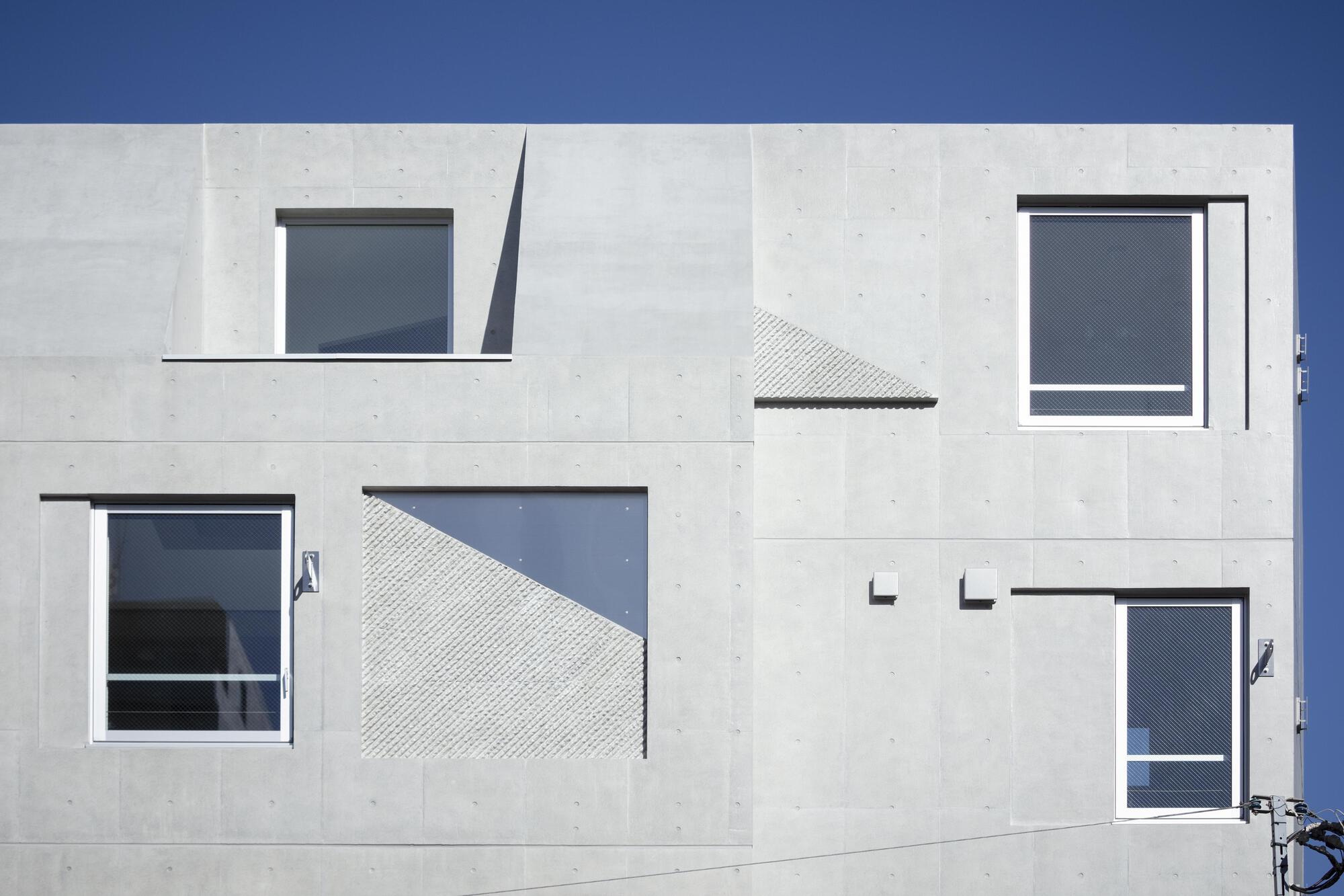 Close view of the concrete facade with offset windows and textured diagonal panels under deep blue sky