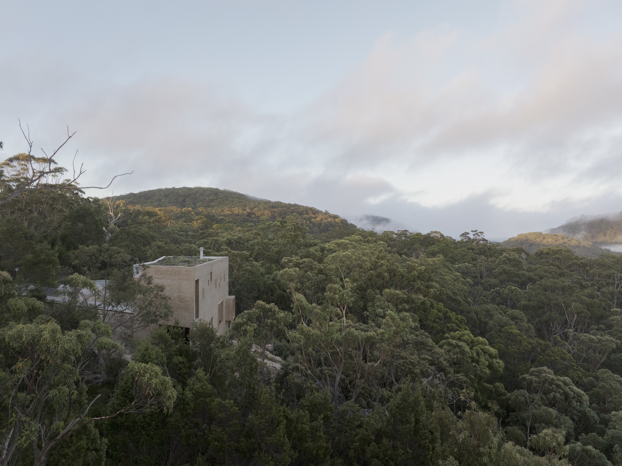 Distant view of the brick tower with a green roof rising from dense forest canopy beneath soft pink clouds