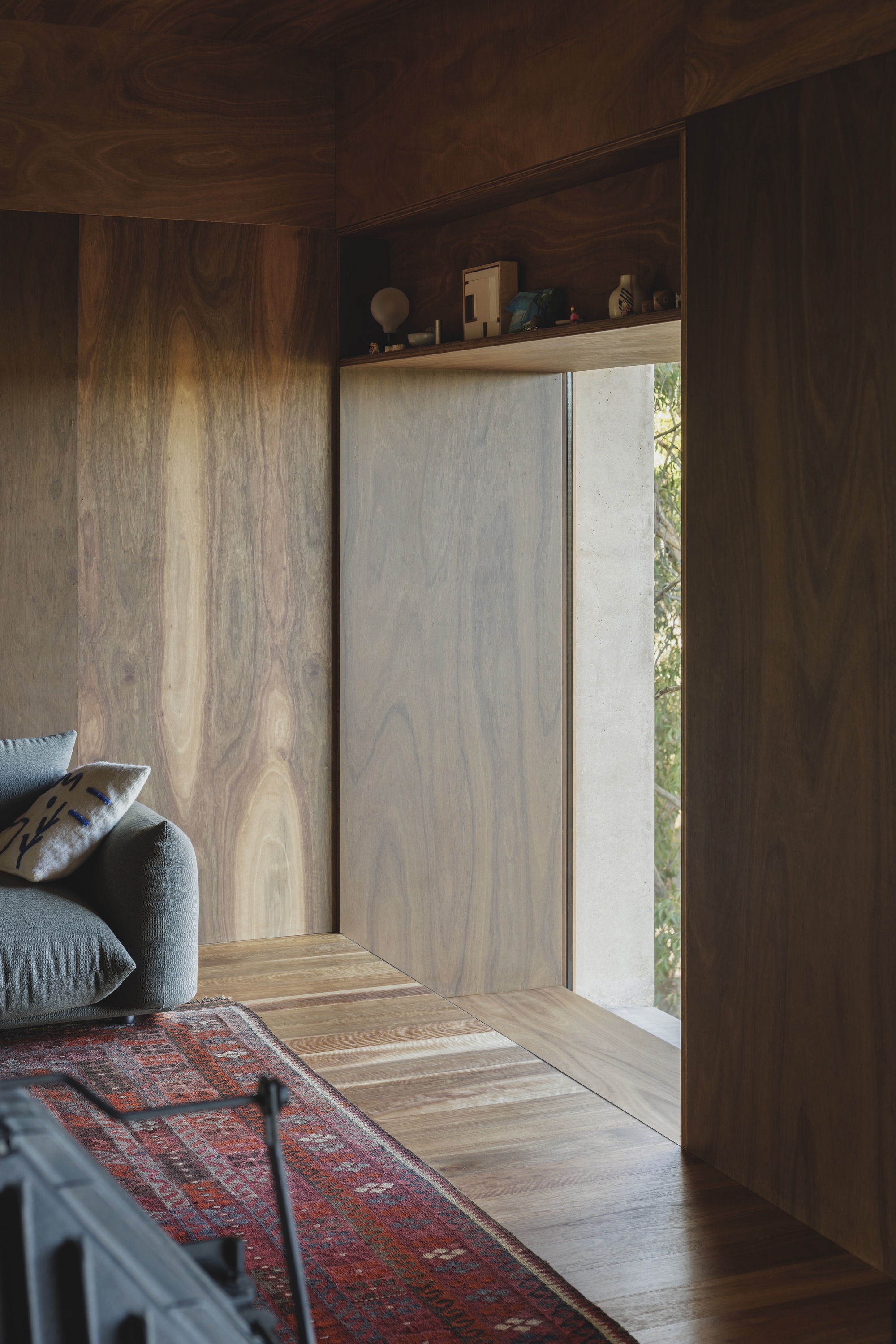 Close-up of the recessed window reveal in figured timber panelling, with a shelf of small objects above and a red rug below