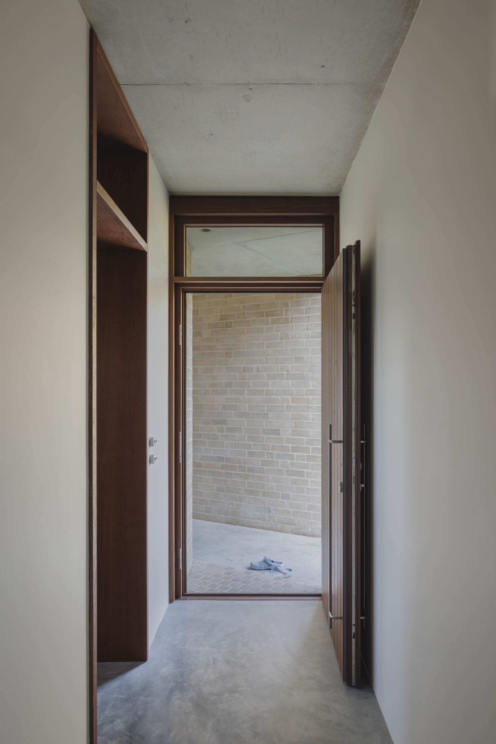 Open timber door framing a pale brick wall and paved covered porch, with a cloth left on the ground