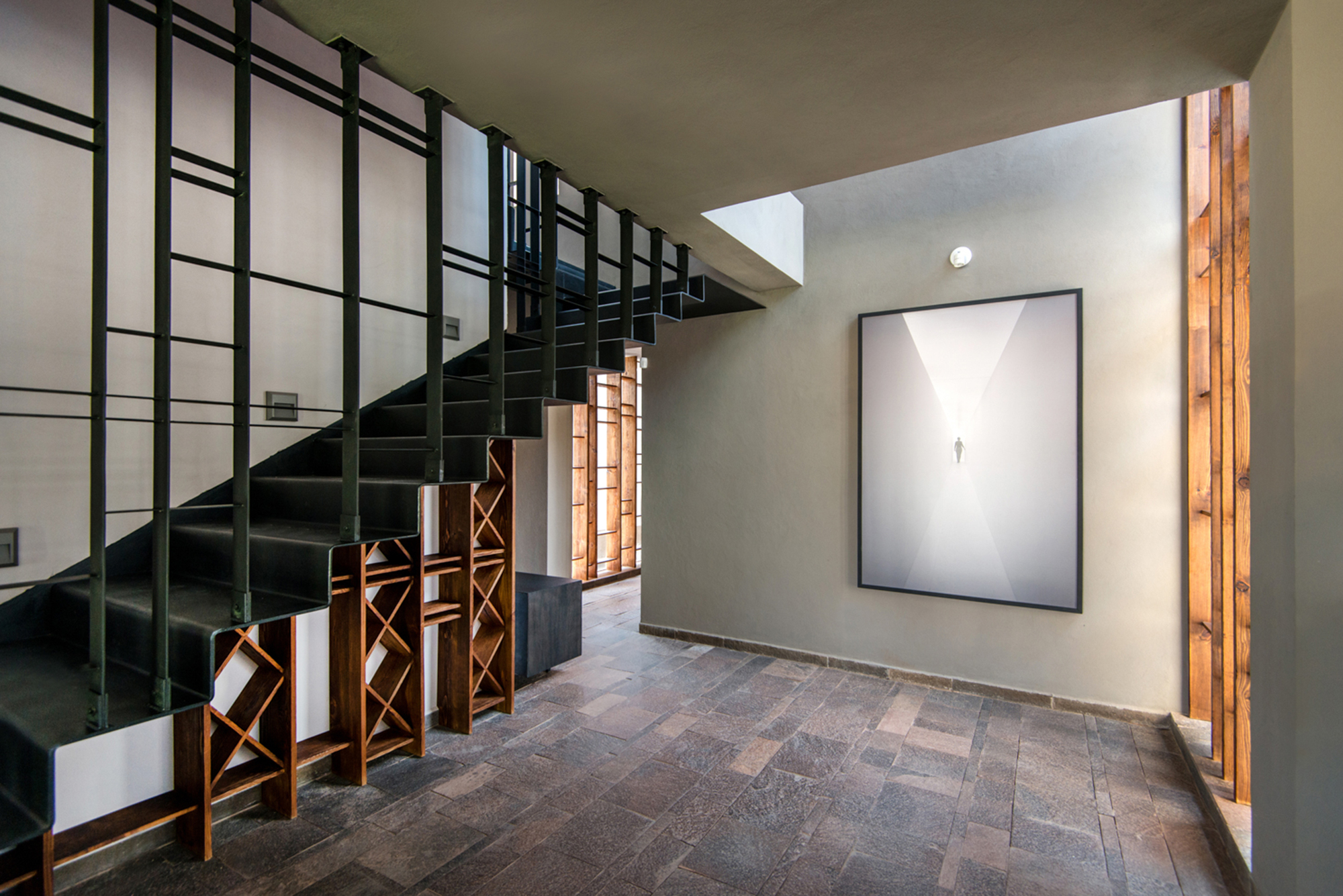 Entry hall with black steel stair, timber lattice base and flagstone floor beside a framed artwork on a grey wall