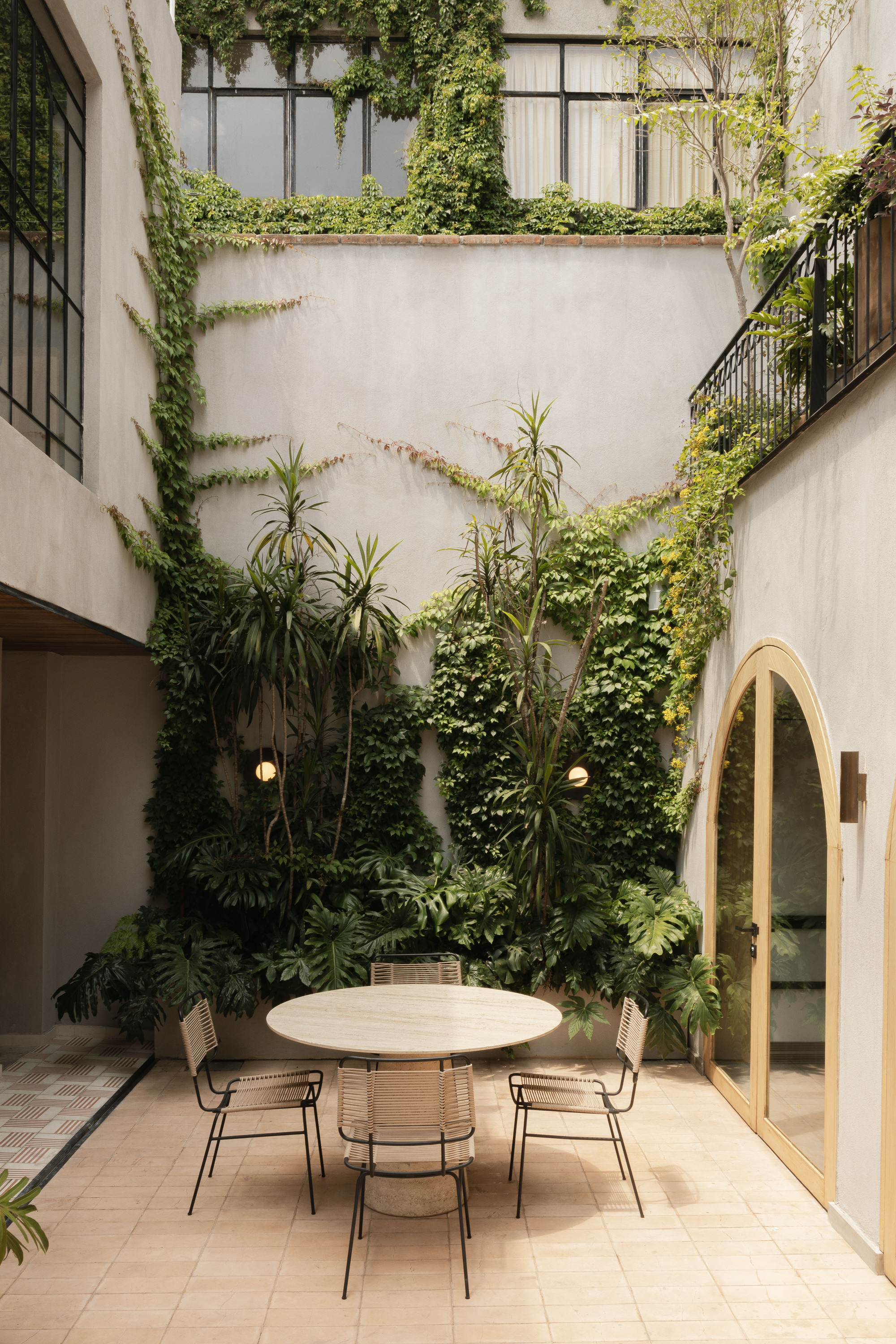 Courtyard dining spot with a round stone table beneath a wall of climbing ivy and tall potted plants