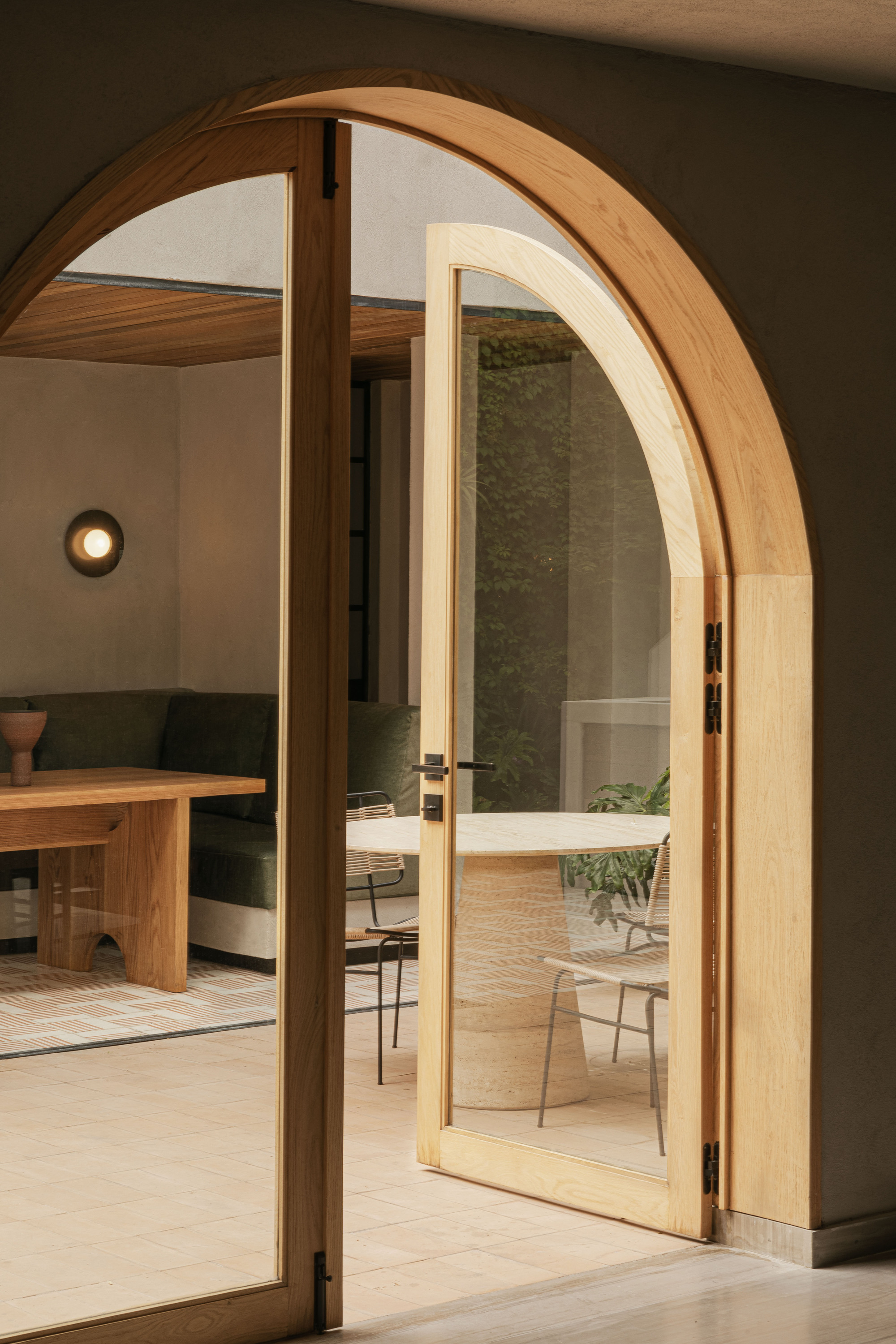 Arched oak-framed glass door standing open onto a sitting area with a round stone table and green sofa
