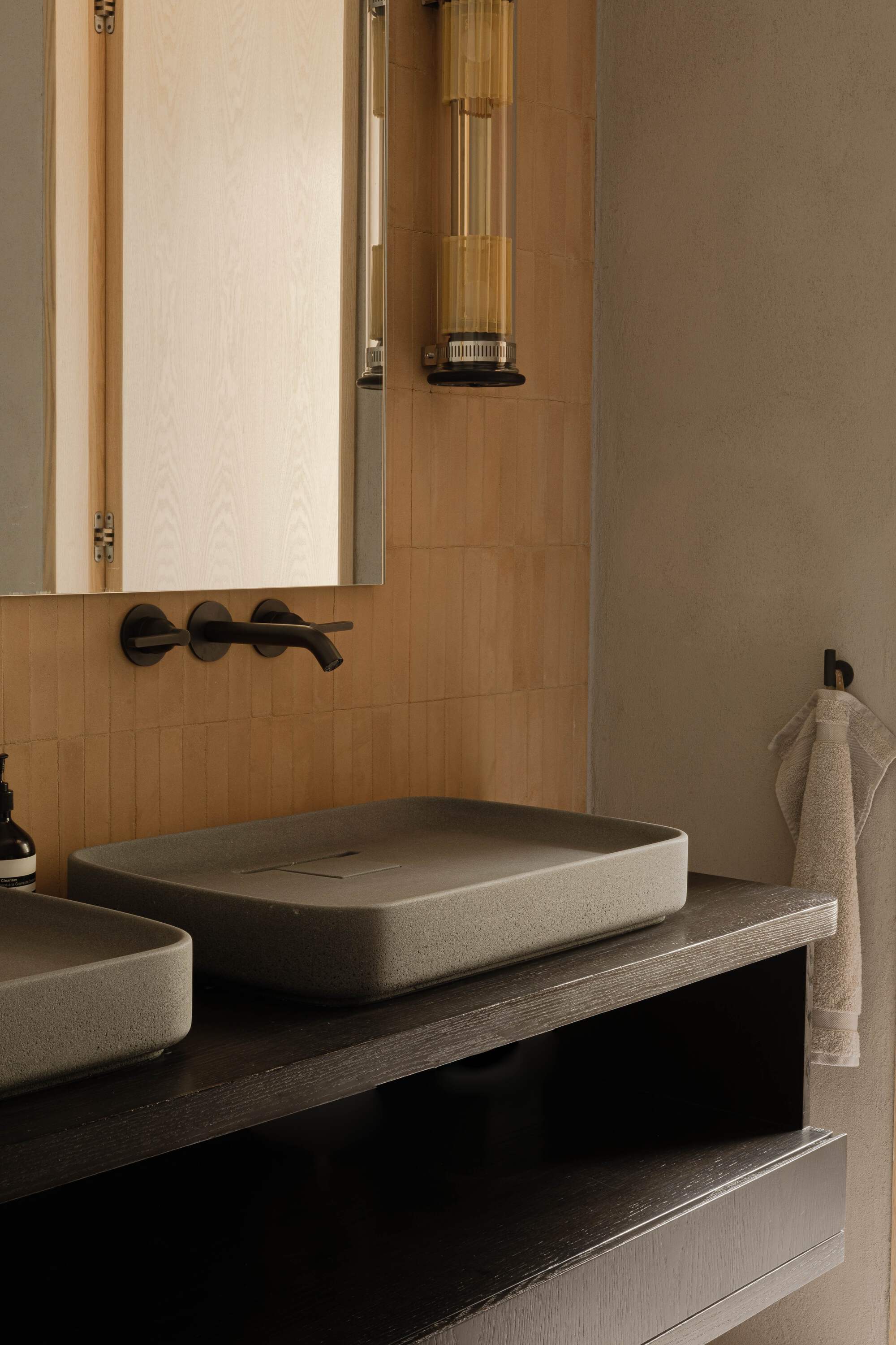 Twin grey stone basins on a dark wood vanity below a mirror cabinet, with a wall-mounted black tap and ochre tile backsplash