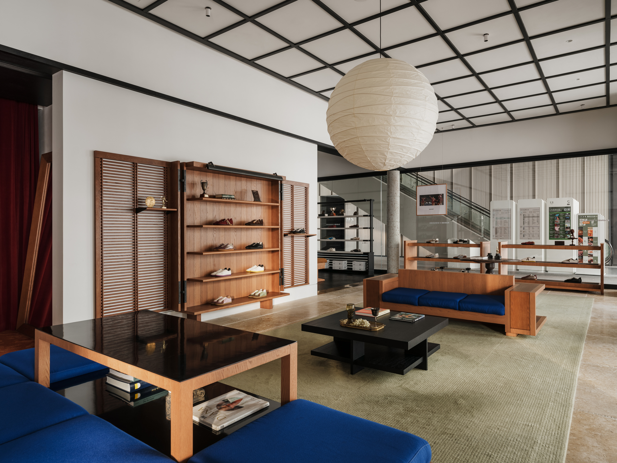 Retail lounge with a paper globe pendant, louvered timber shelving and blue cushioned benches around a black lacquer table in soft daylight